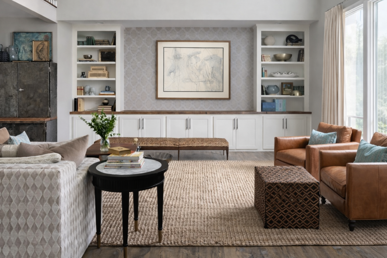 Coastal-inspired living room with classic furniture, built-in shelves, a large window with ivory drapery, and a framed artwork on the wall. Built-in bookshelves are artfully styled with books and collectibles.