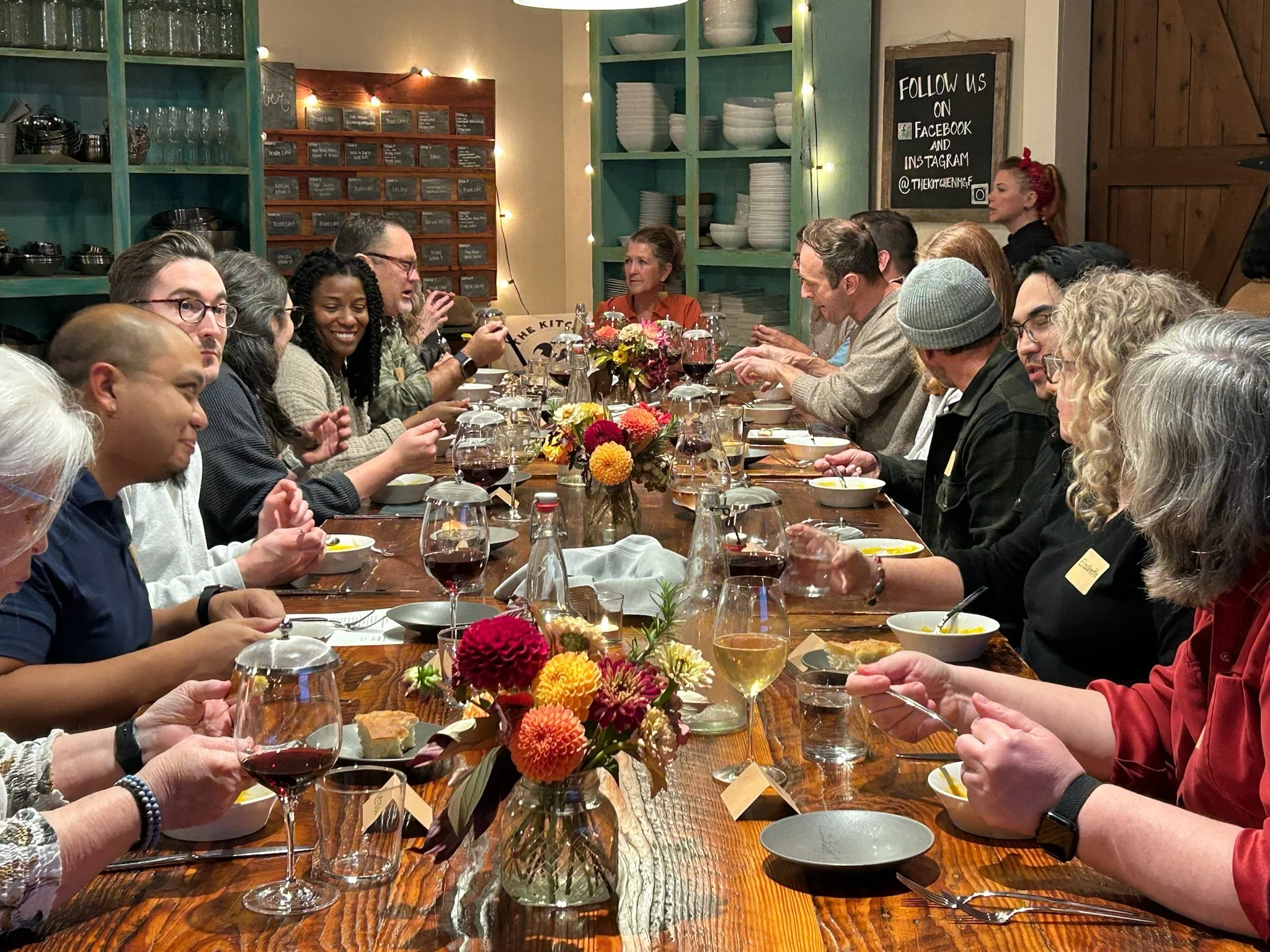 Two musicians performing indoors with a woman singing into a microphone and a man playing acoustic guitar, against a wooden barn-style wall.