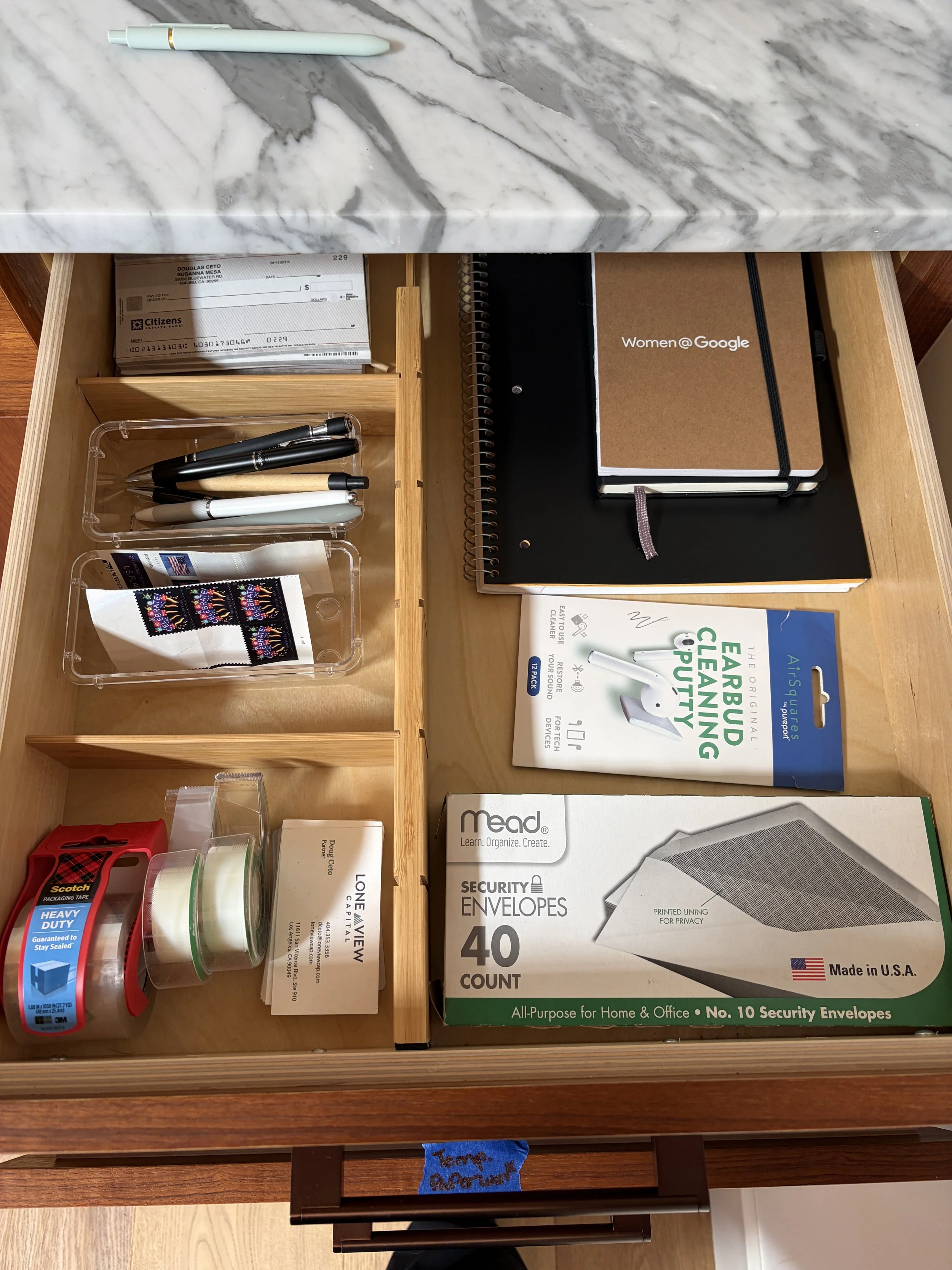 An open wooden desk drawer containing office supplies representing a well organized and minimal drawer for eco method interiors decluttering and home organizing service