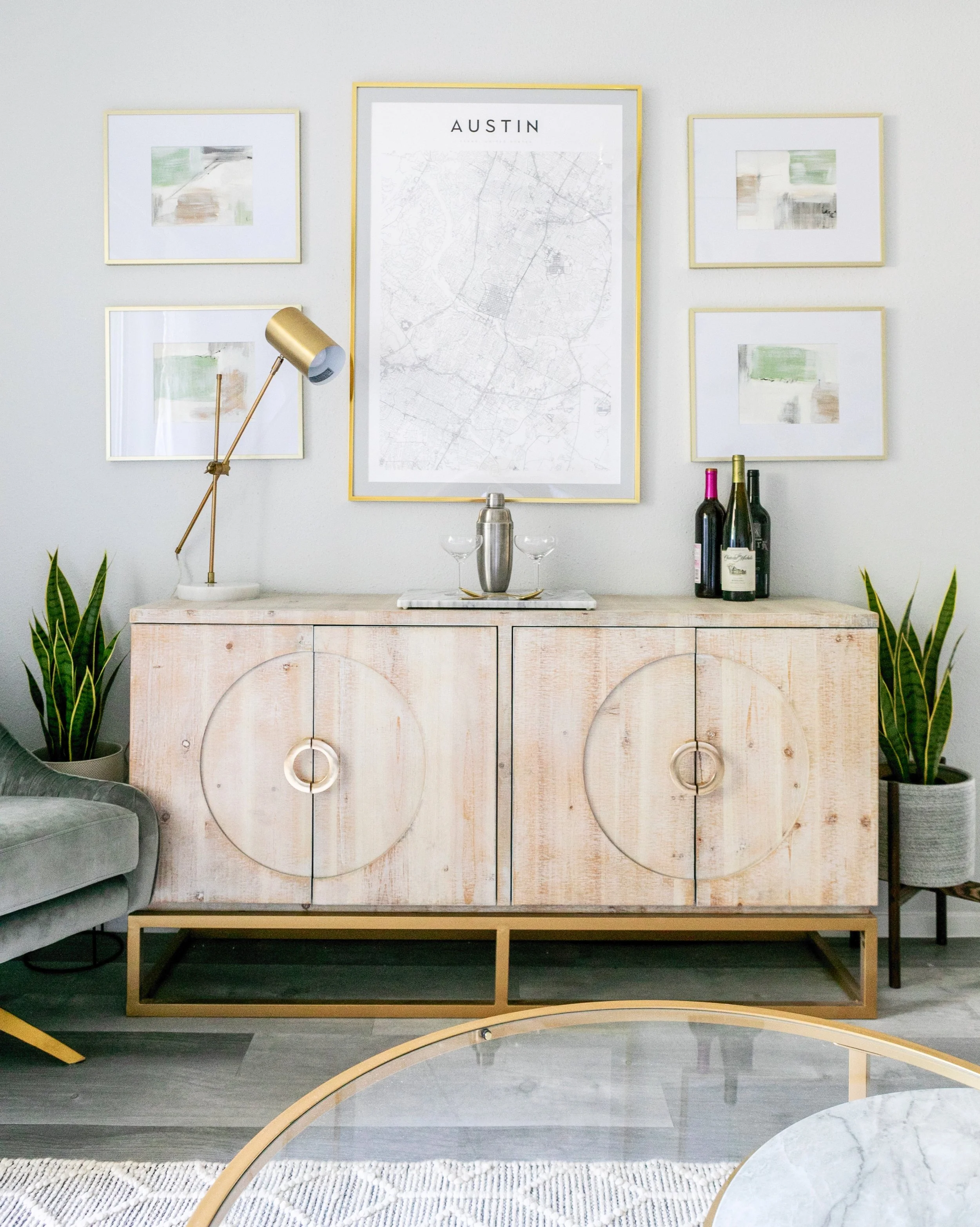 Modern living room with a wooden cabinet, abstract artwork, and a large map of Austin, Texas on the wall, accompanied by a gold and marble bar cart, Showcasing a model unit apartment space designed for maximum ROI