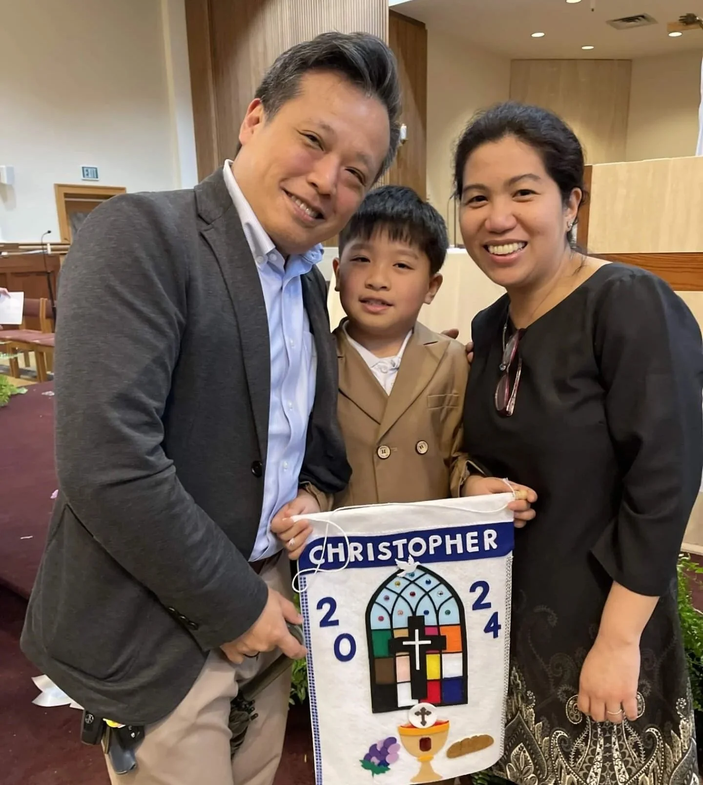 Family of mother, father and young boy in the church holding up his First Communion banner and smiling