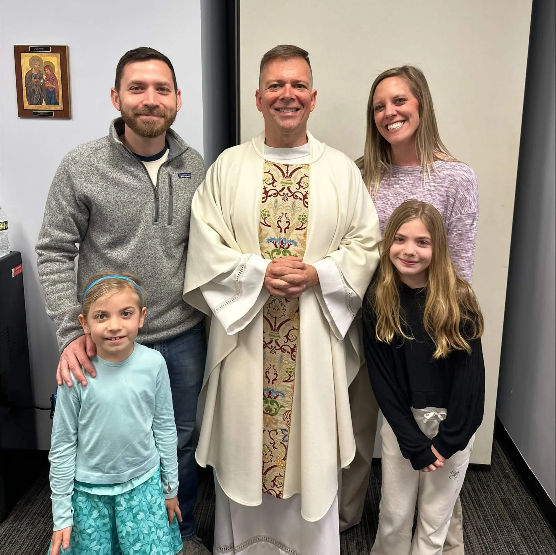 Family of mother, father, and two school aged girls pictured with Father A J, smiling