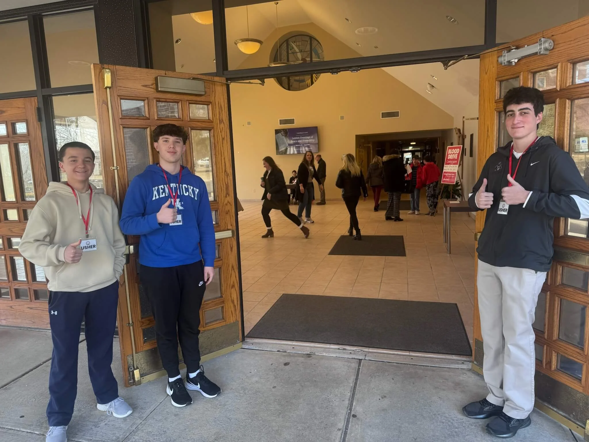 Young men wearing sweatshirts and "Usher" lanyards, smiling at front door