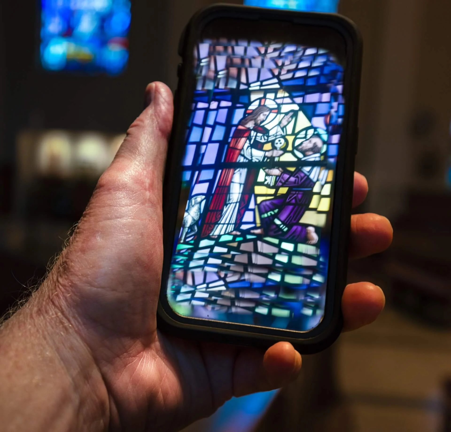 Hand holding up cell phone against wall with painted chat bubble containing a social media "like" icon