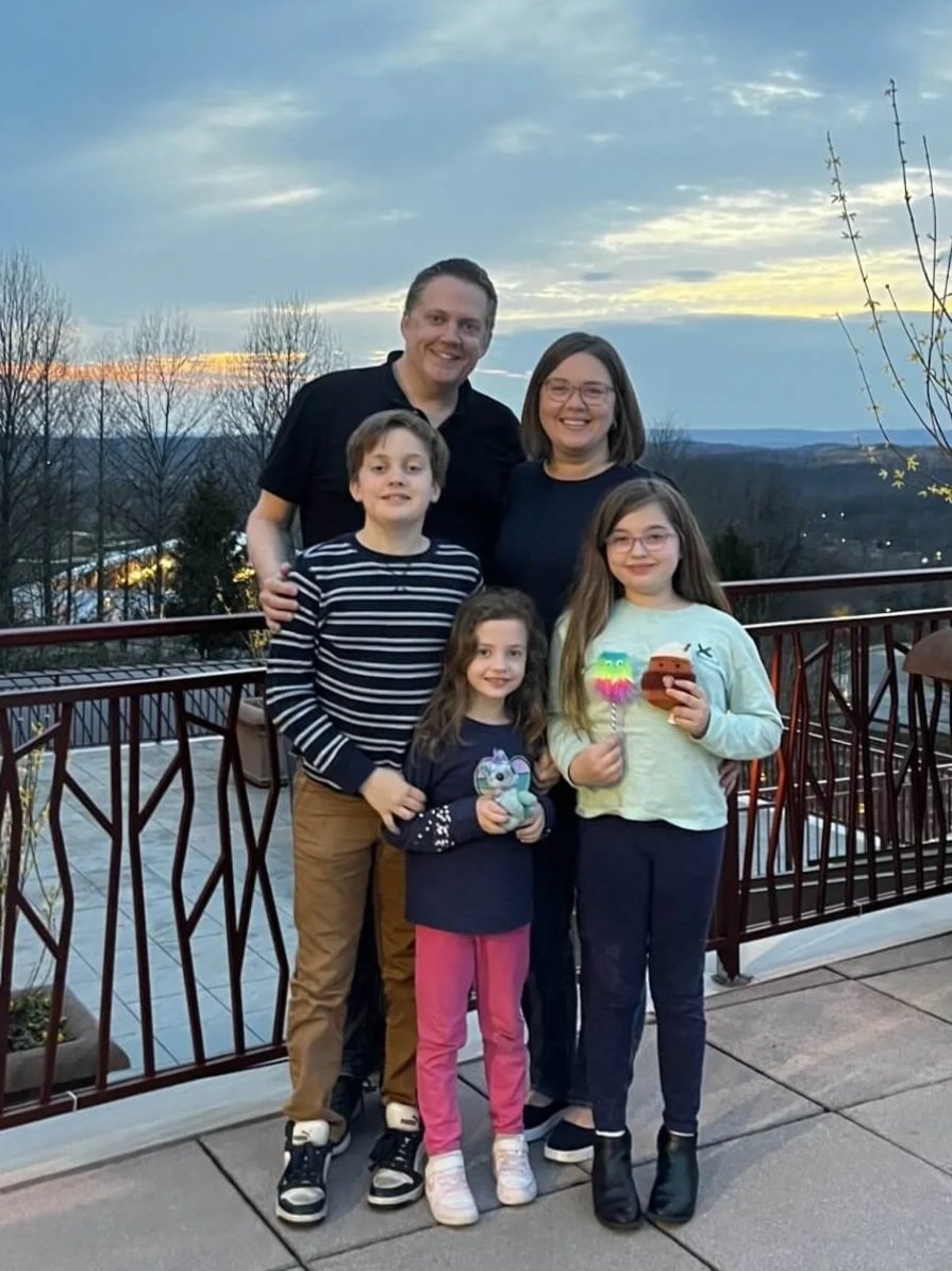 Family of mother, father, and three school aged children pictured with Father Mike, smiling