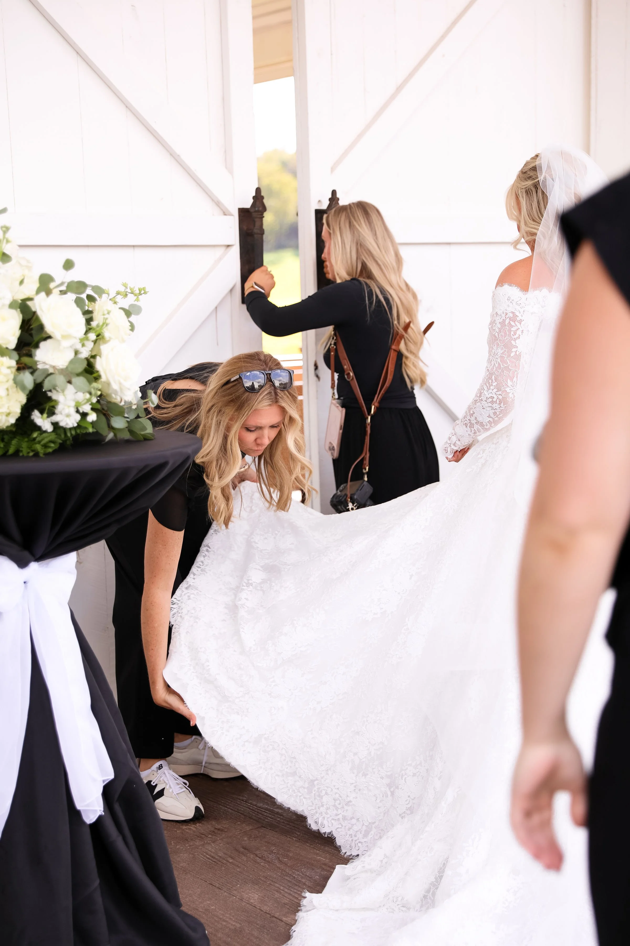 Women preparing a bride's wedding dress inside a barn.