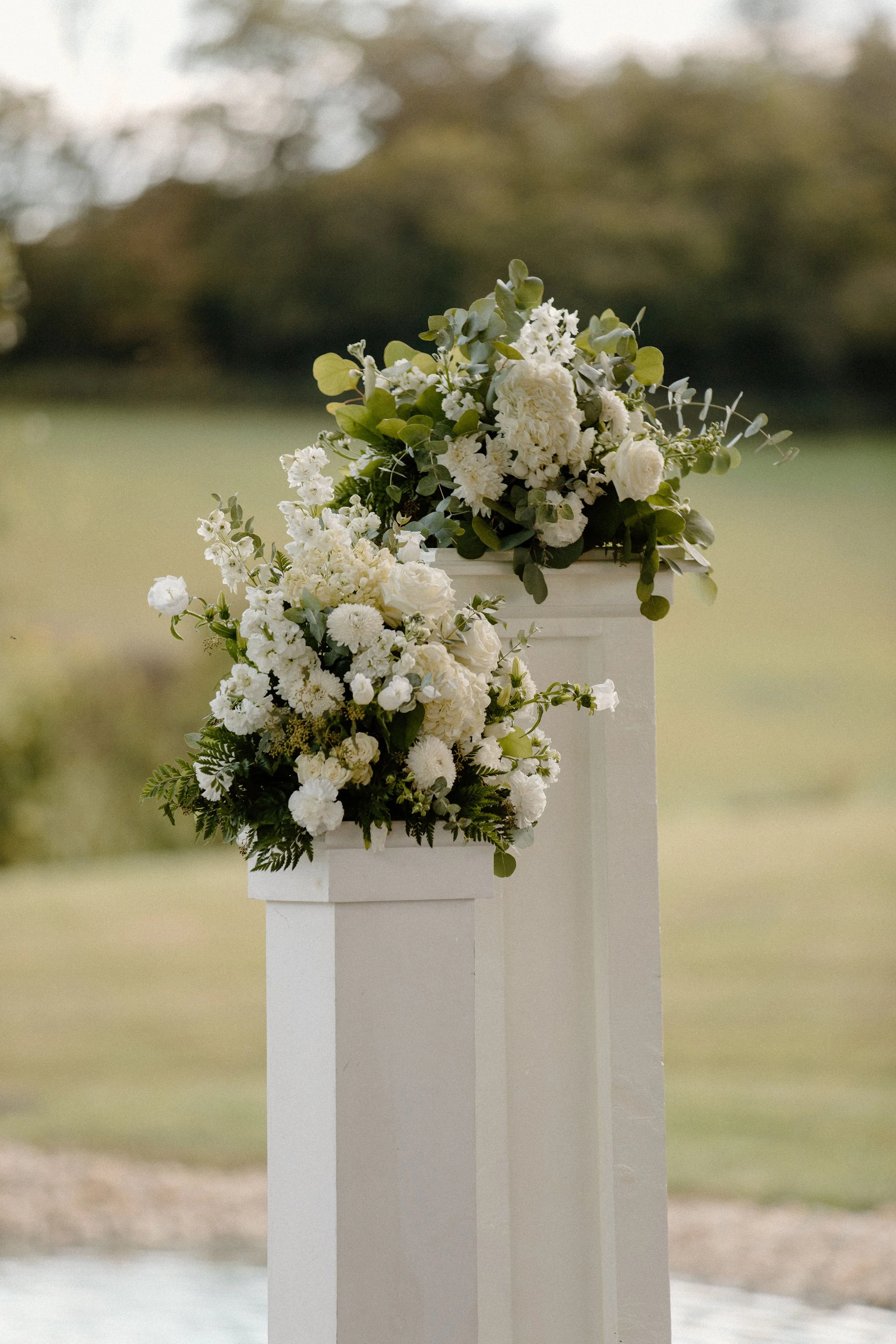 A bride in a white wedding gown holding a bouquet of white roses and greenery, flanked by bridesmaids in blue dresses holding similar bouquets.