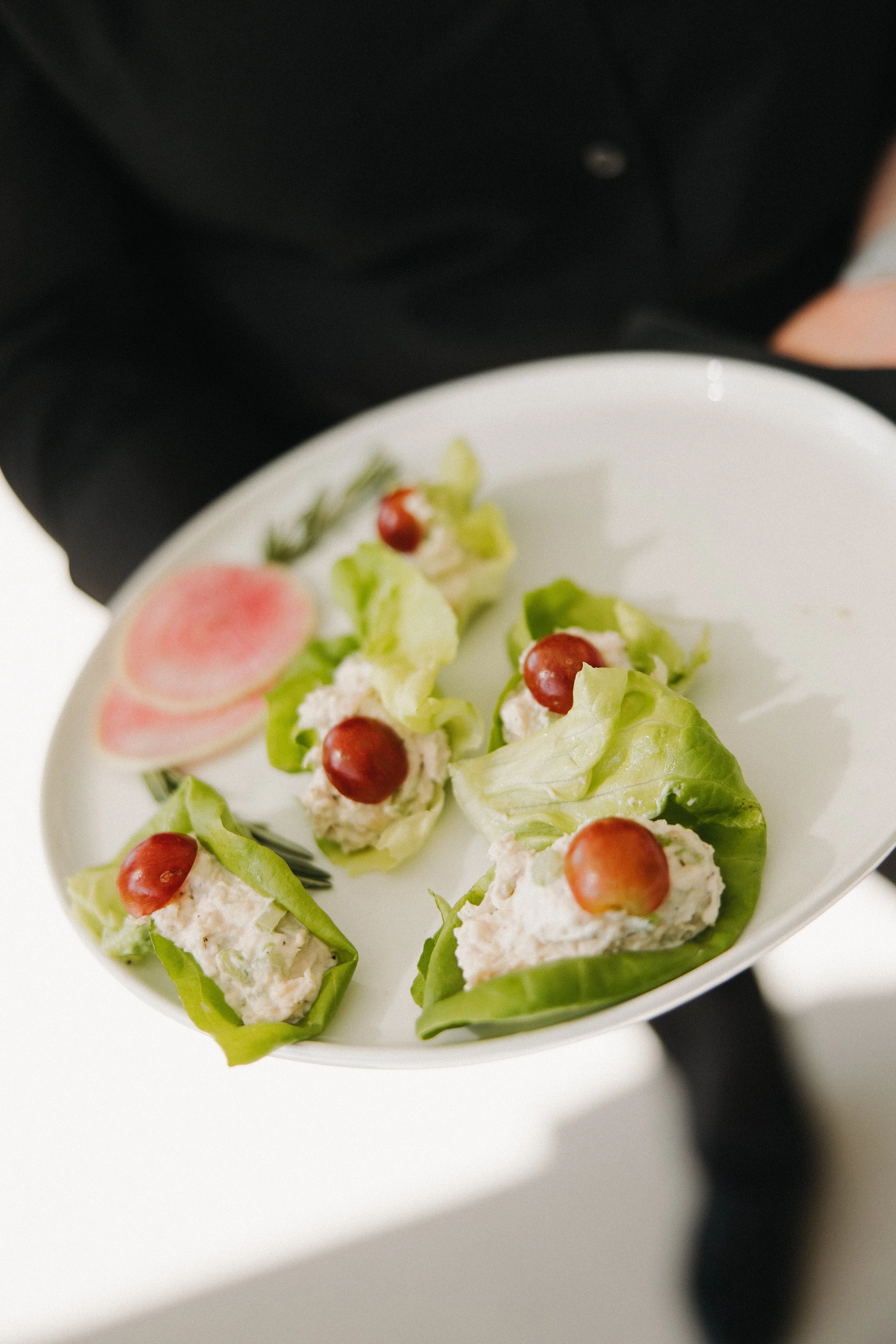 Plate with lettuce wraps filled with chicken salad and topped with grapes, accompanied by cucumber and radish slices.