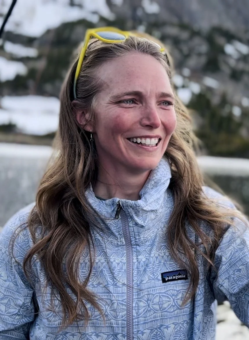 Good therapist in Leadville. Therapist in Lake County. Counselor in Lake County. A smiling woman with long, wavy hair, wearing a light blue patterned jacket and outdoors with a blurred background of snow-covered trees.
