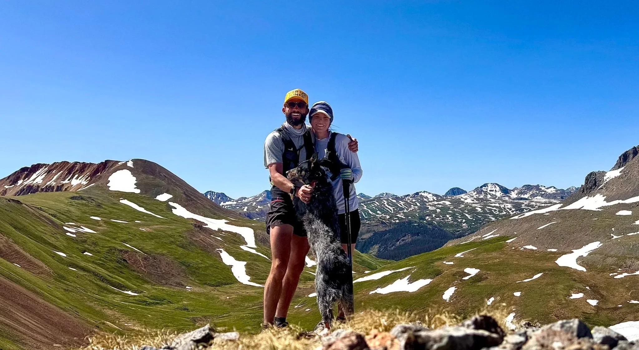 Good counselor near me. Takes insurance. Therapist in Leadville. Therapist in Colorado. A couple with a dog on a mountain trail with snow patches and green slopes under a clear blue sky.