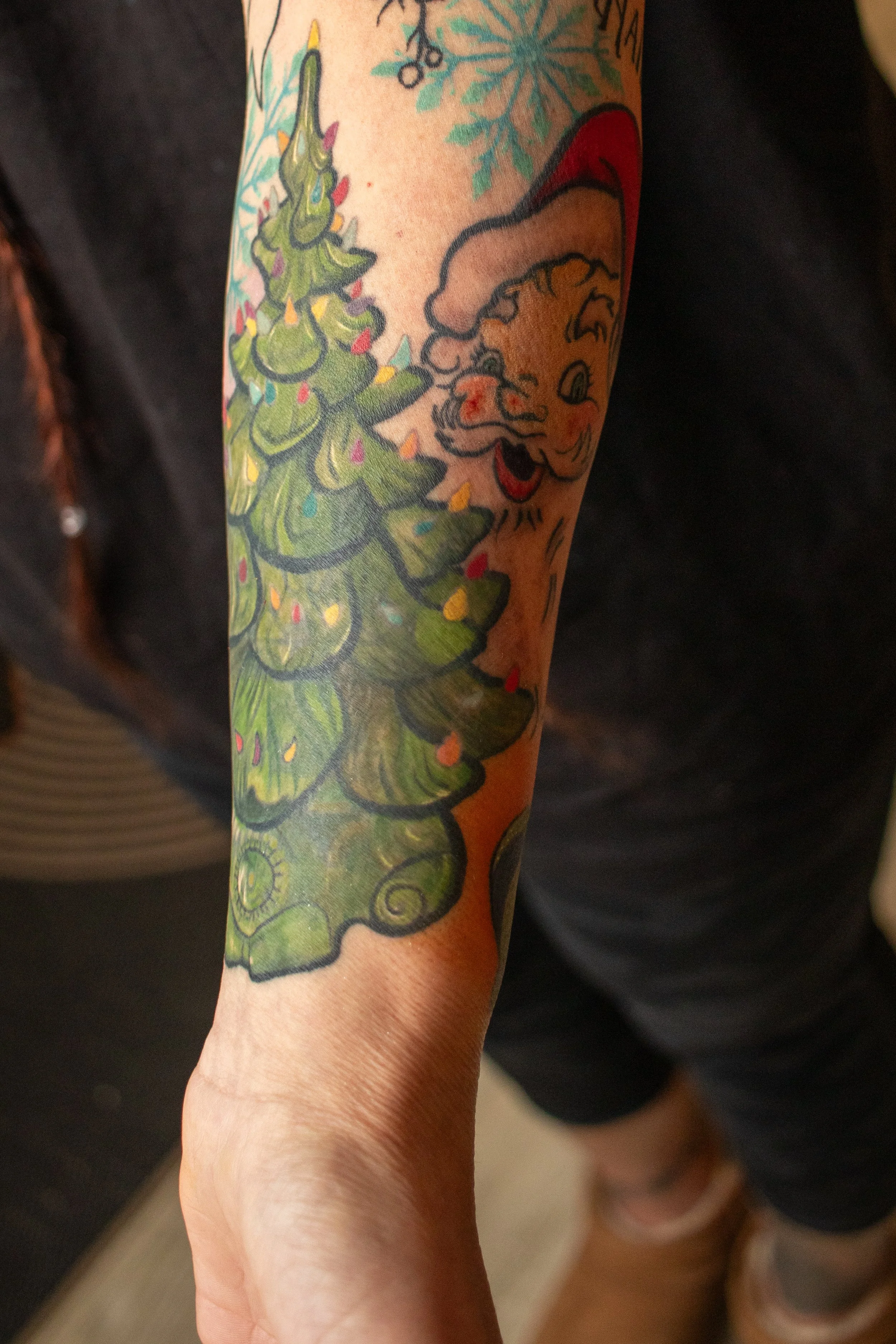 Tattoo of a Christmas tree and a Santa face on a person's forearm.