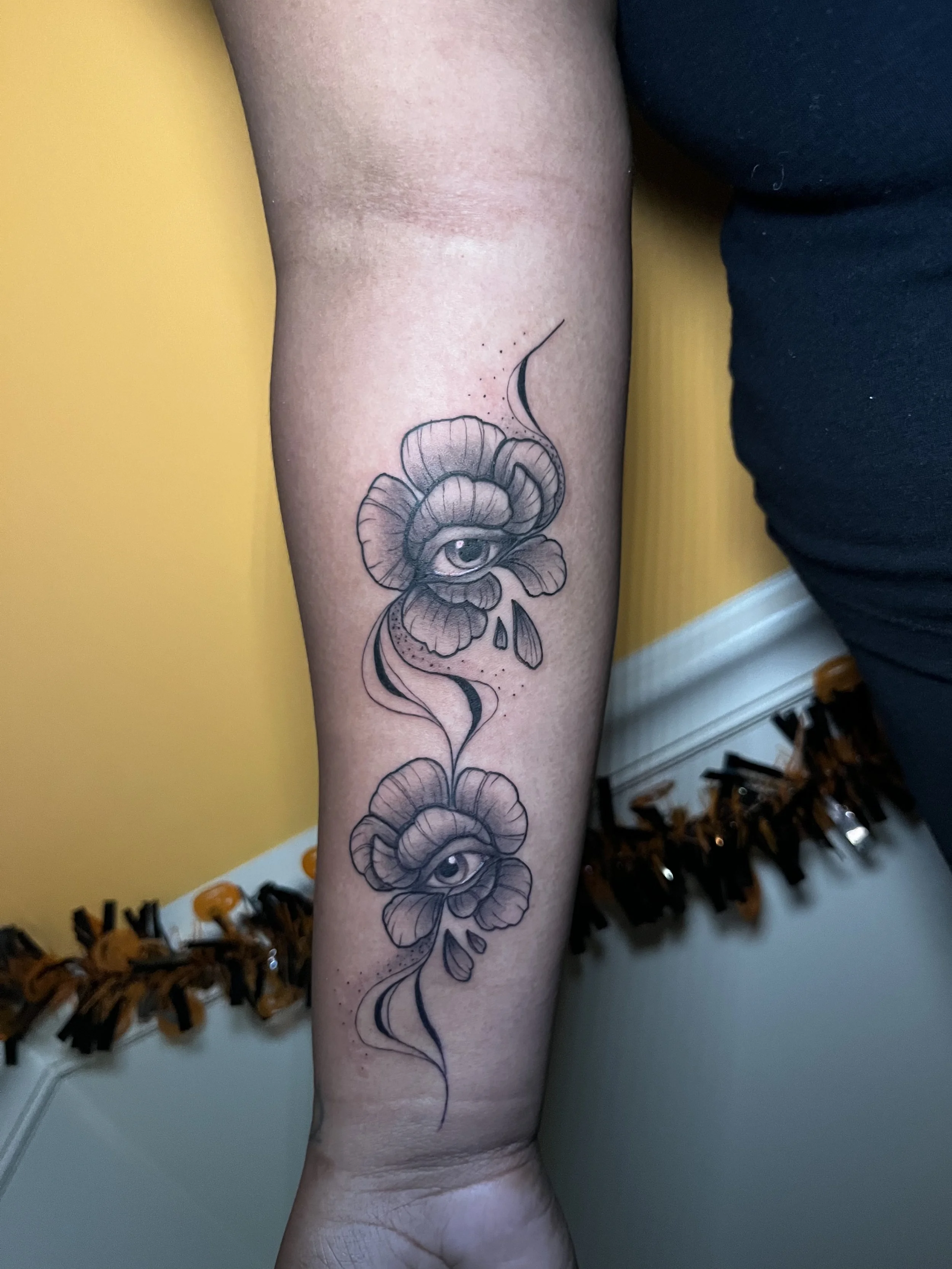 Tattoo of eyes and flowers on a person's forearm.