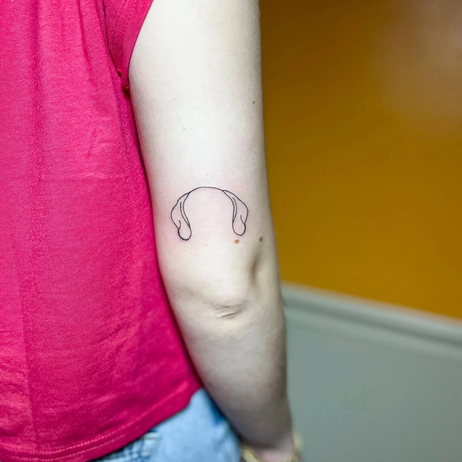 Tattoo of a simple line drawing of dog ears on a person's upper arm.