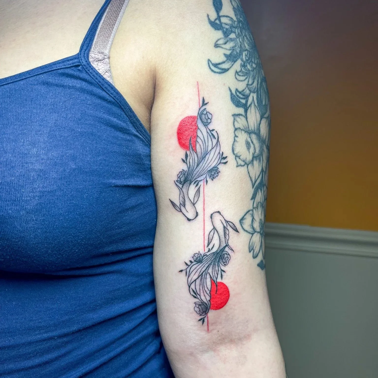 Tattoo of two swans with flowing feathers, connected by a thin line, and two red circles on the person's upper arm.