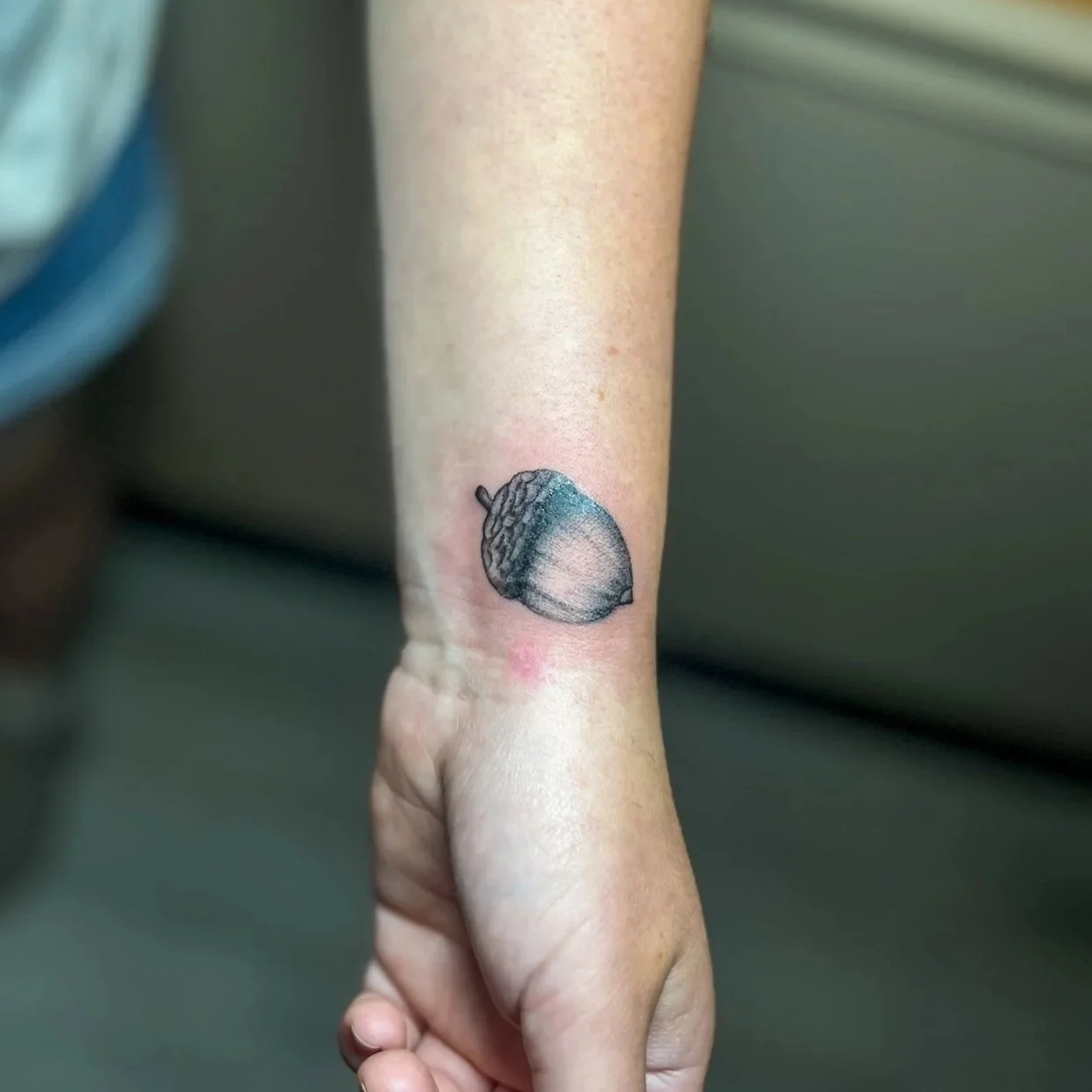 Tattoo of an acorn on a person's inner wrist.