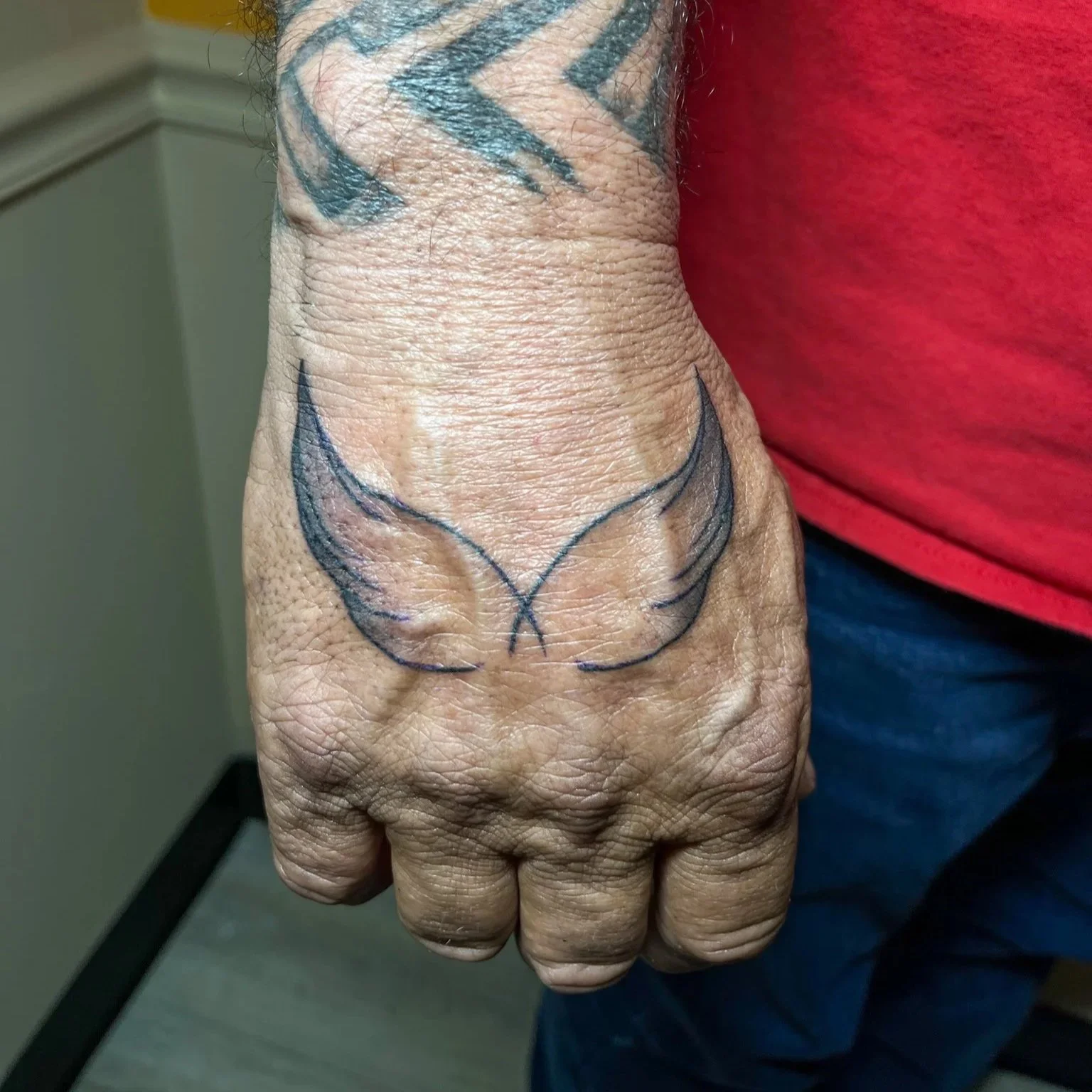 A tattoo of butterfly wings on the person's hand, with the wings outlined in black ink and shaded in light colors.