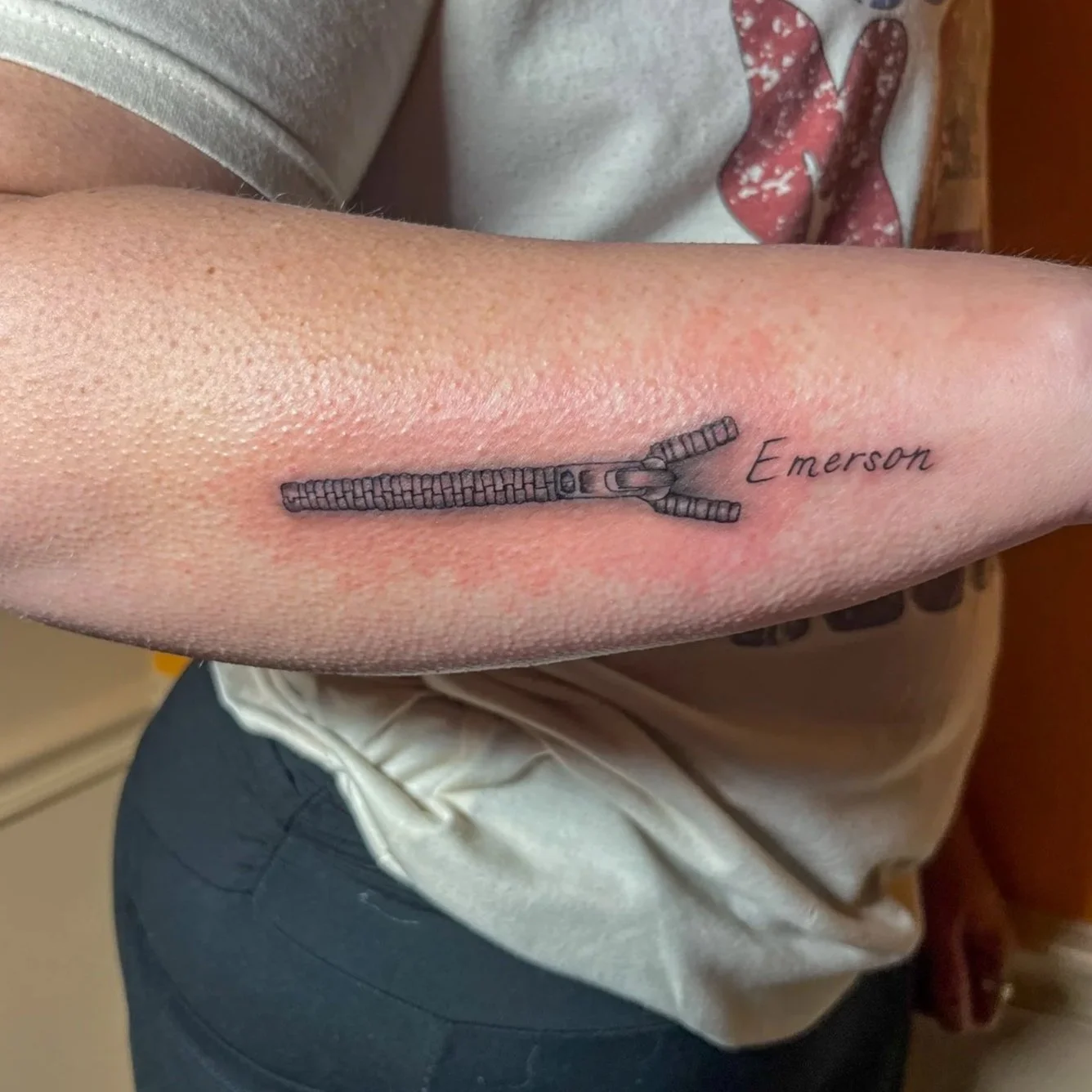 Tattoo of a zipper with the name Emersom on the inner forearm.