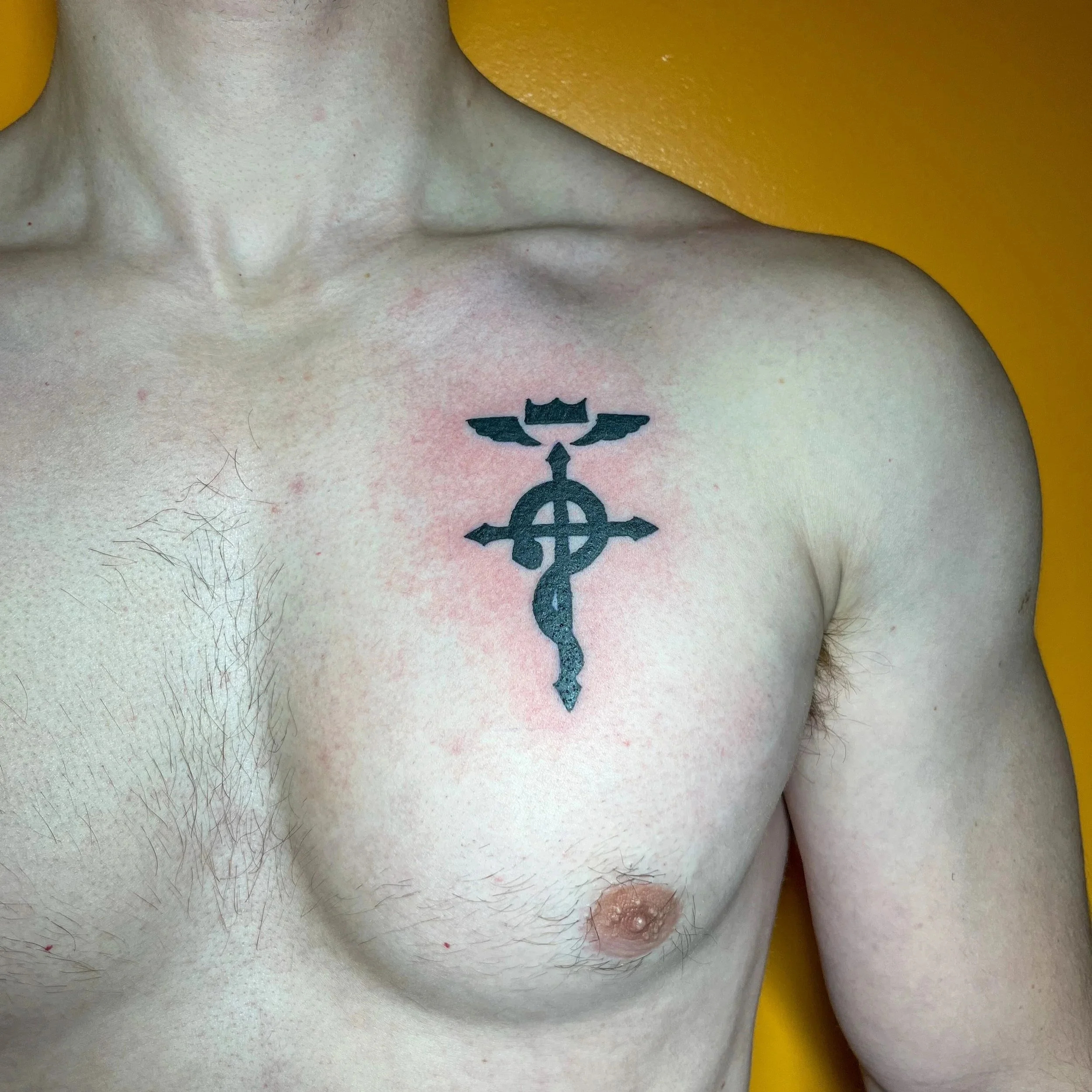Tattoo of a black cross with wings and a crown on the upper chest of a shirtless person.