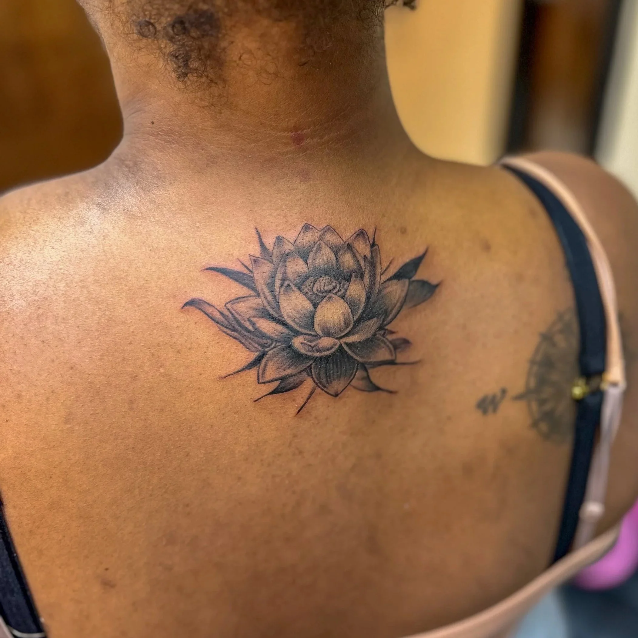 Black and gray ink tattoo of a detailed lotus flower on a person's upper chest.