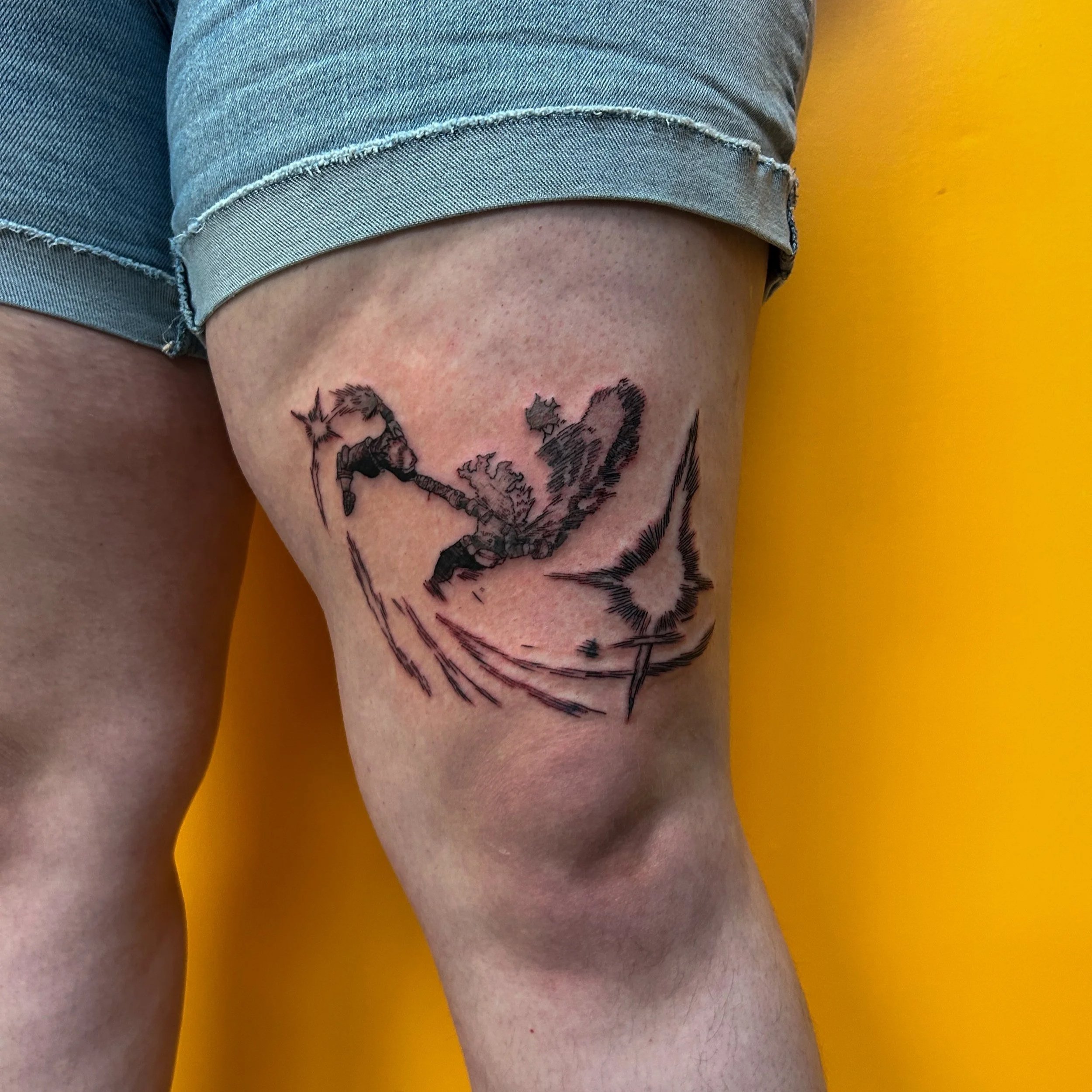 Tattoo of a fantasy character wielding a weapon, fighting a large feline, on upper thigh of person wearing denim shorts against a yellow background.