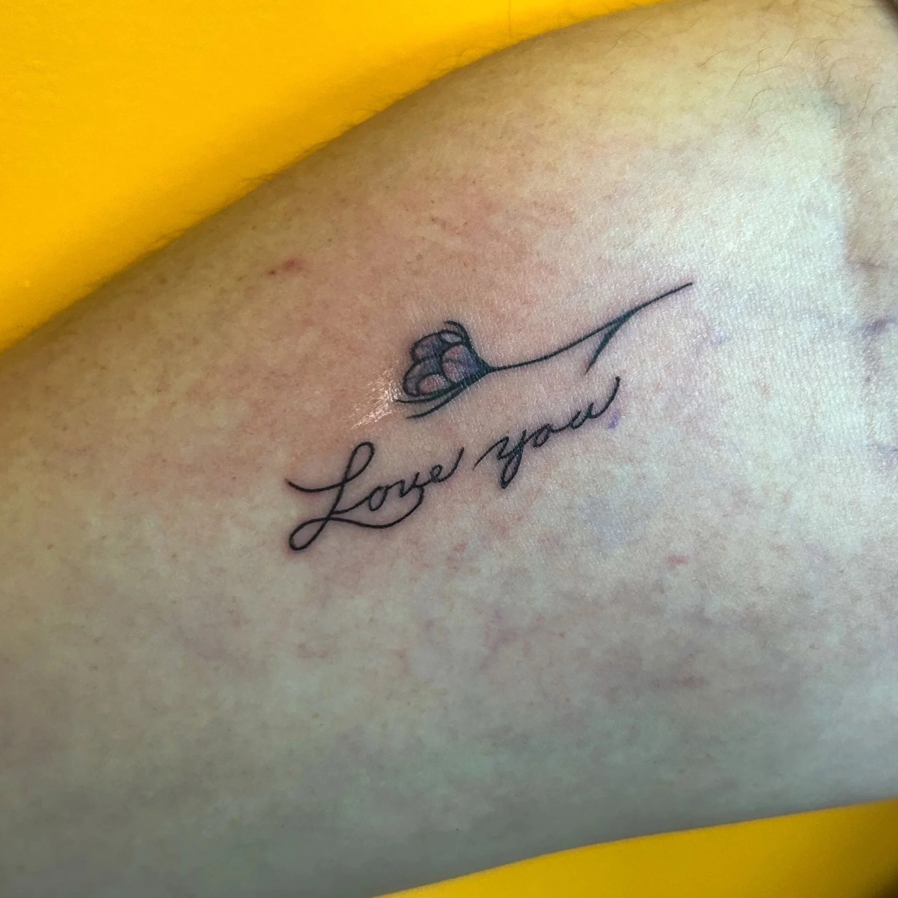 A close-up of a tattoo on skin featuring a flower and the words "Love you" in cursive script.