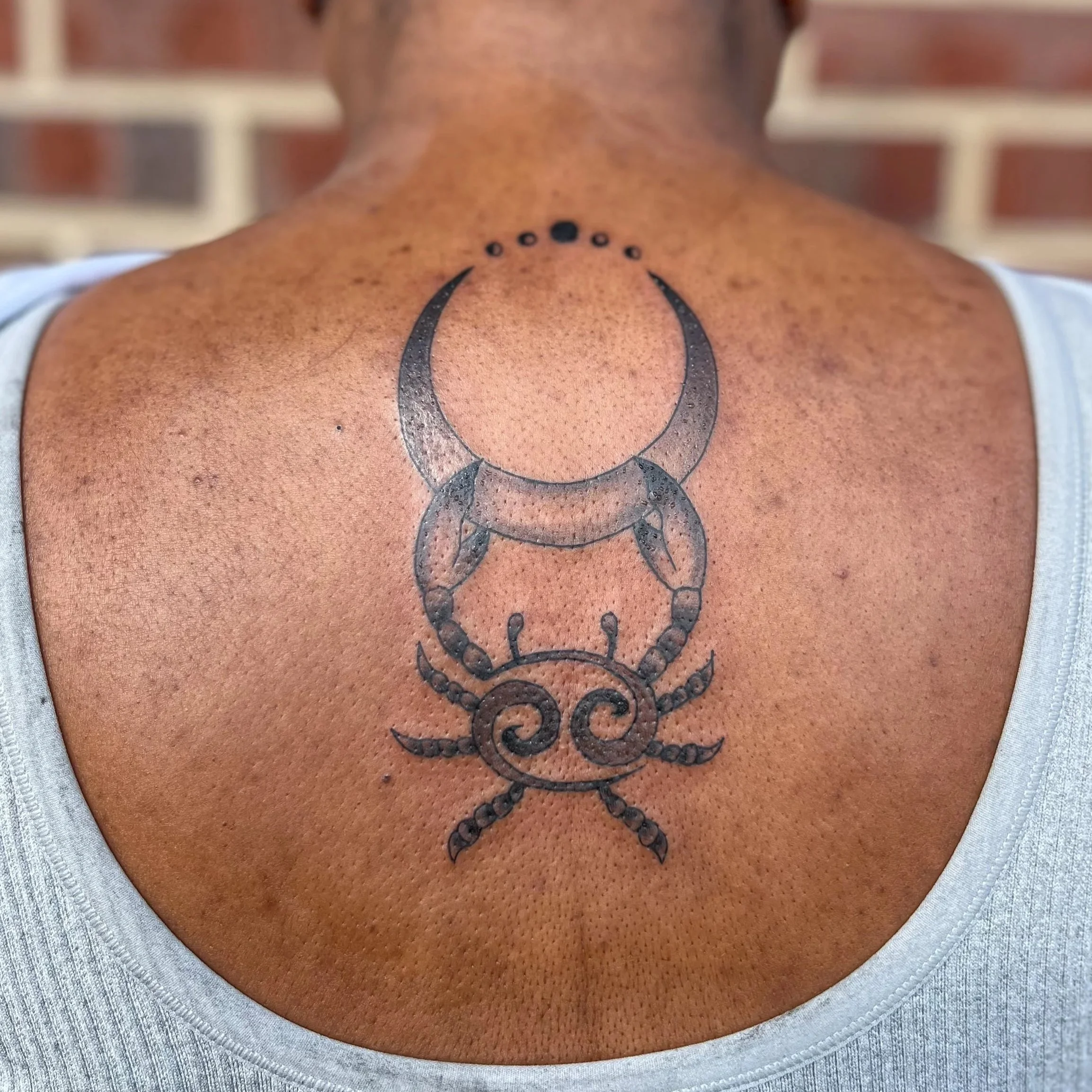 Tattoo of a crescent moon, a crab, and celestial dots on a person's upper back.