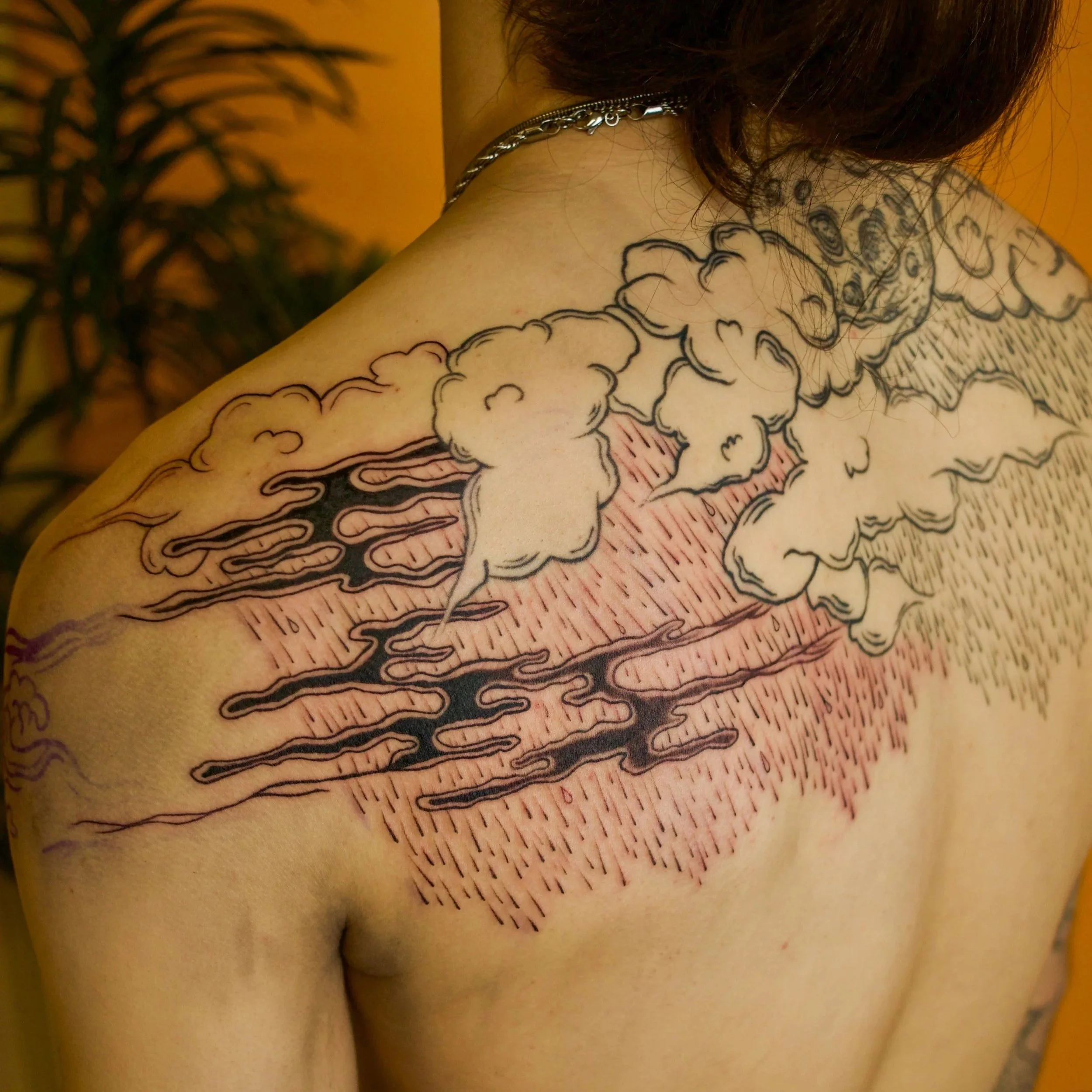Tattoo of a stylized cloud with rain and smoke on a person's shoulder and upper back.