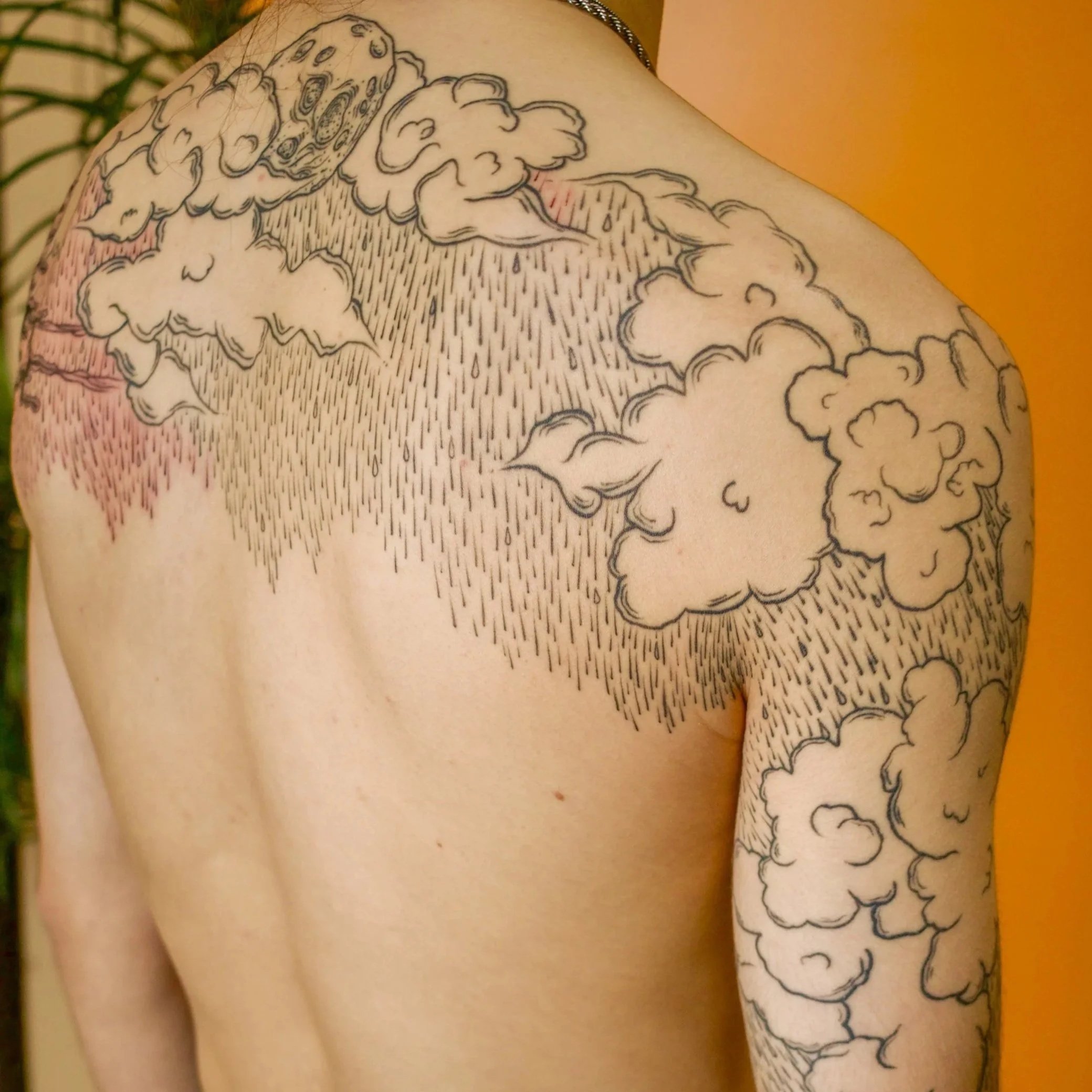 Tattoo of clouds and rain on a person's shoulder and arm.