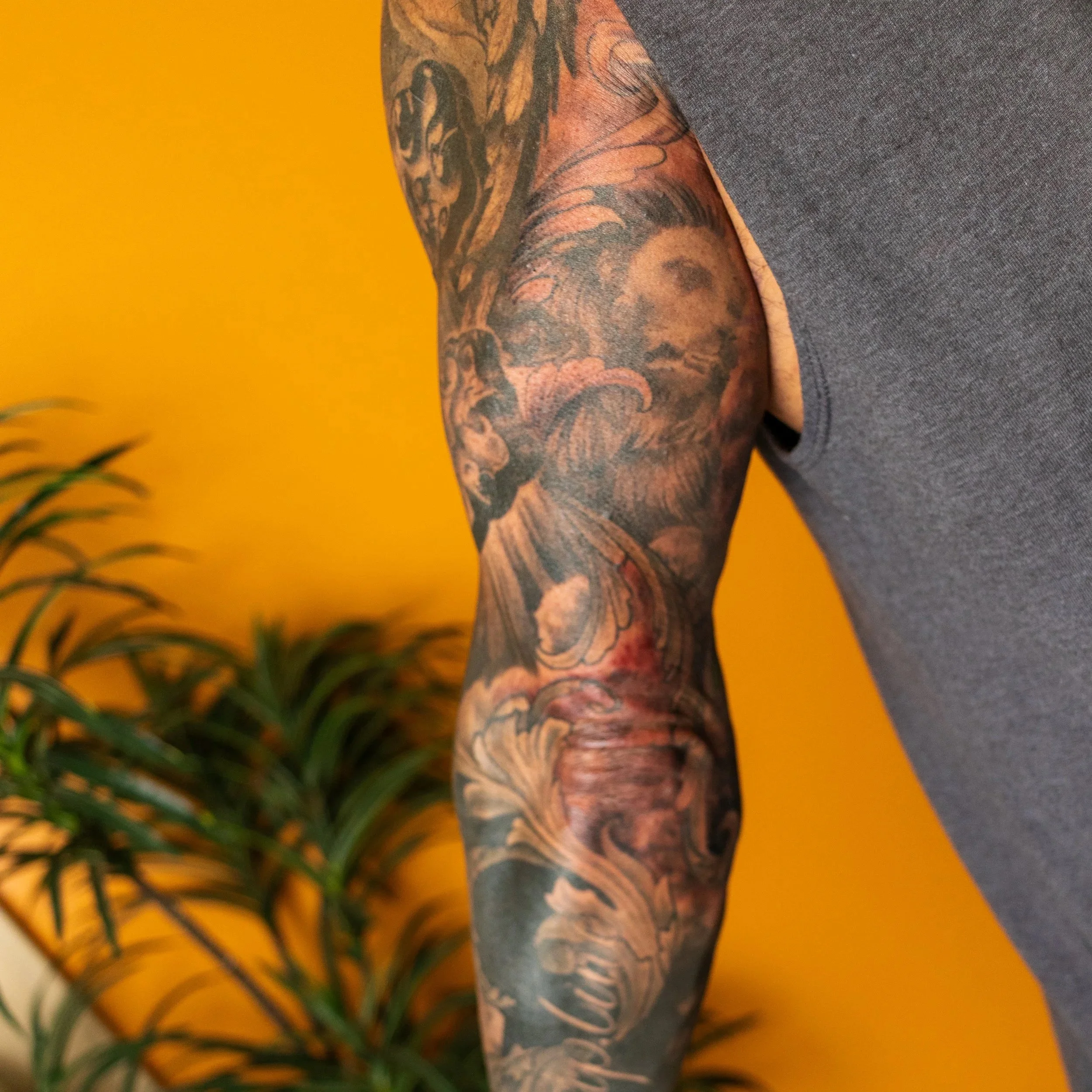 Close-up of a person's arm with a detailed colorful sleeve tattoo, standing against a yellow background.