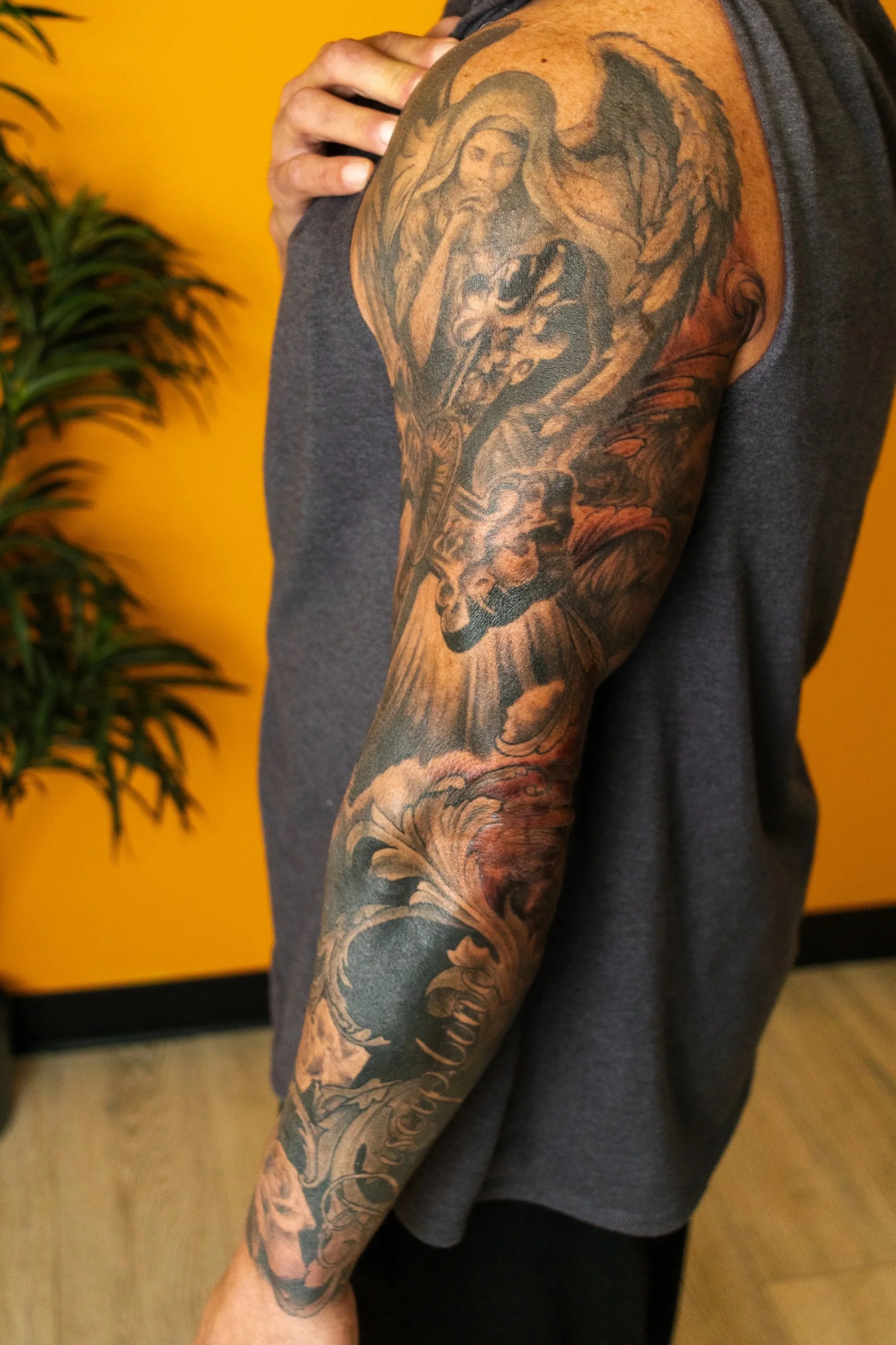 Tattoo of a religious figure, likely the Virgin Mary, with rays of light, a sword, and a skull on the person's upper arm.