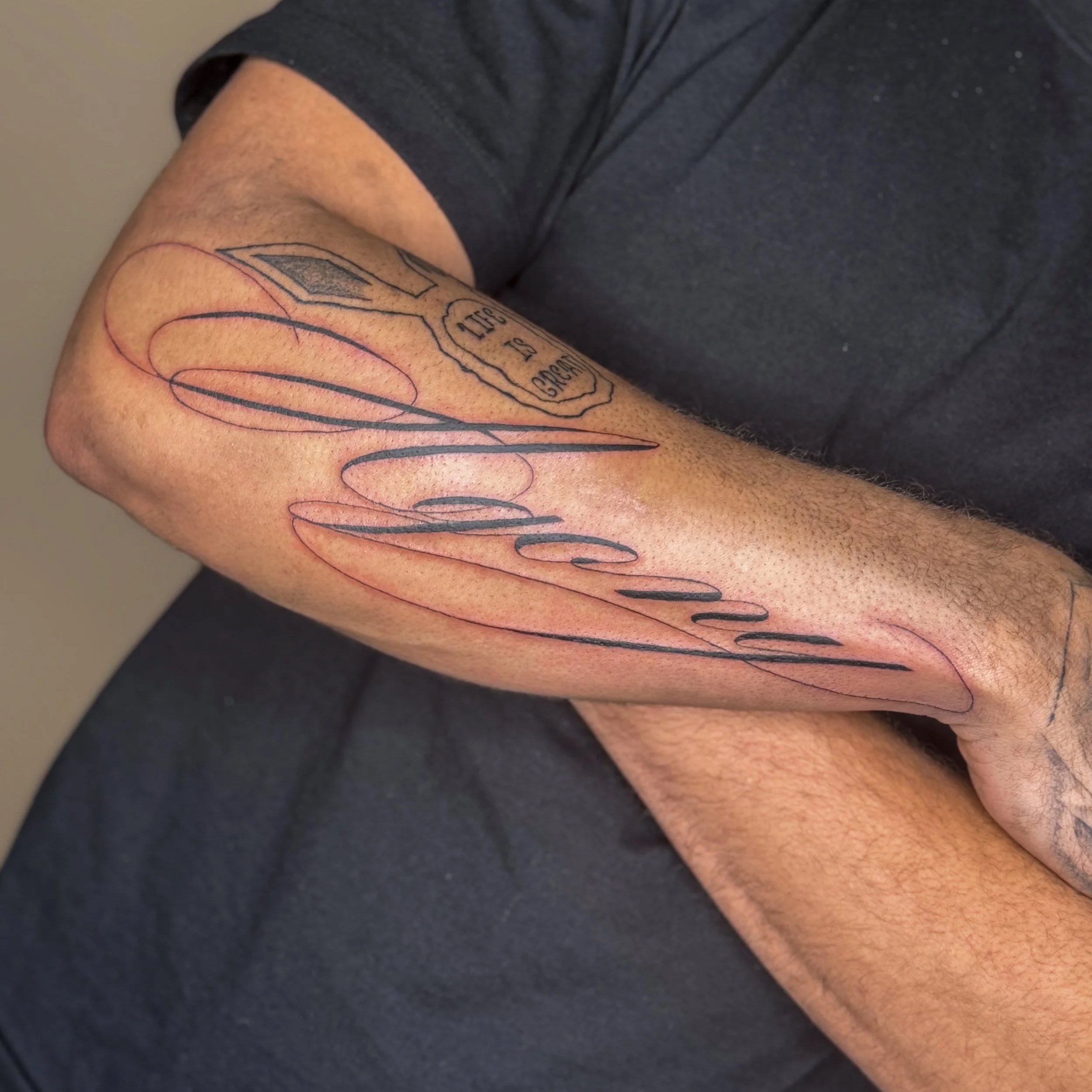 Close-up of a person's arm with a fresh tattoo featuring cursive text.
