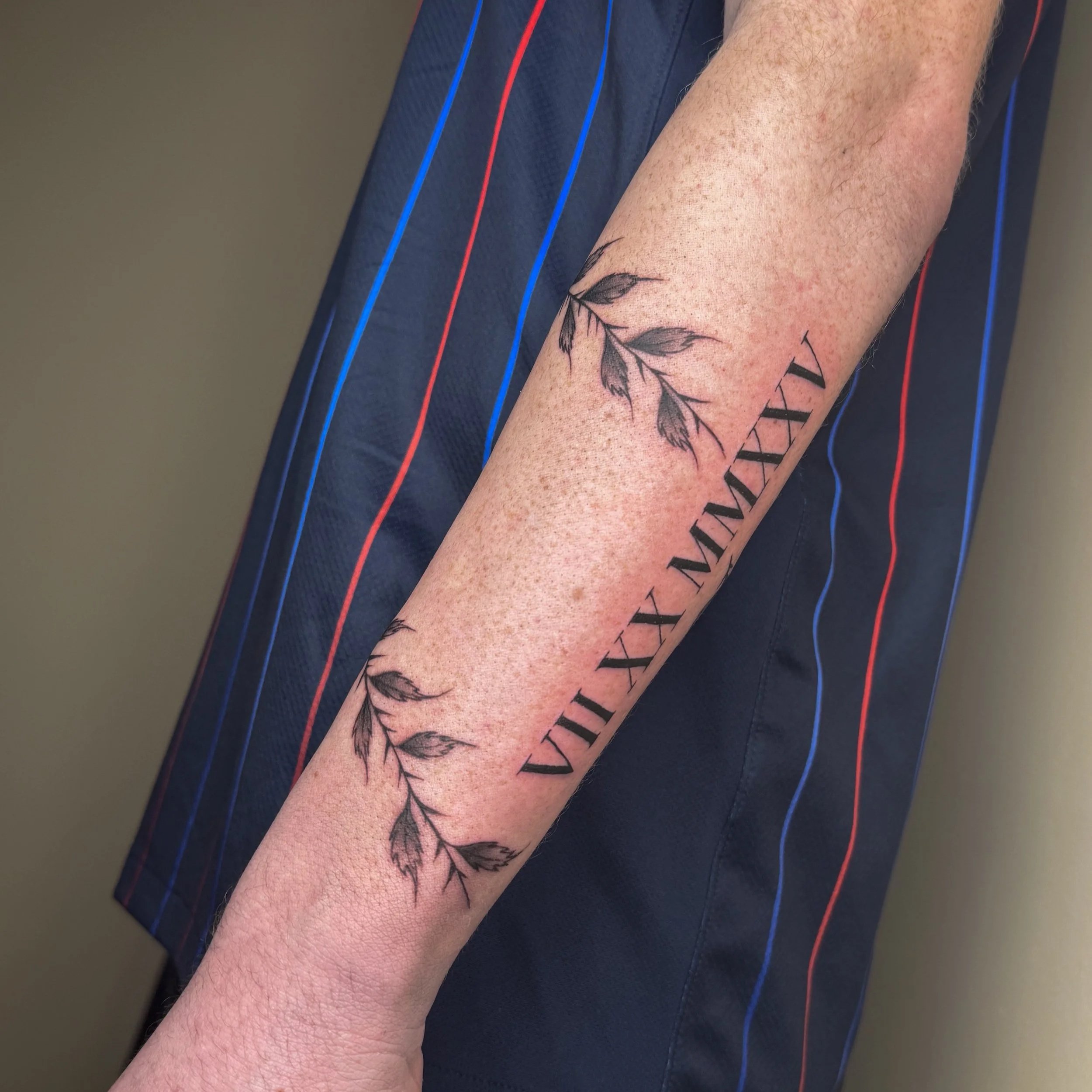 Tattoo of ivy leaves and Latin Roman numerals on person’s forearm.