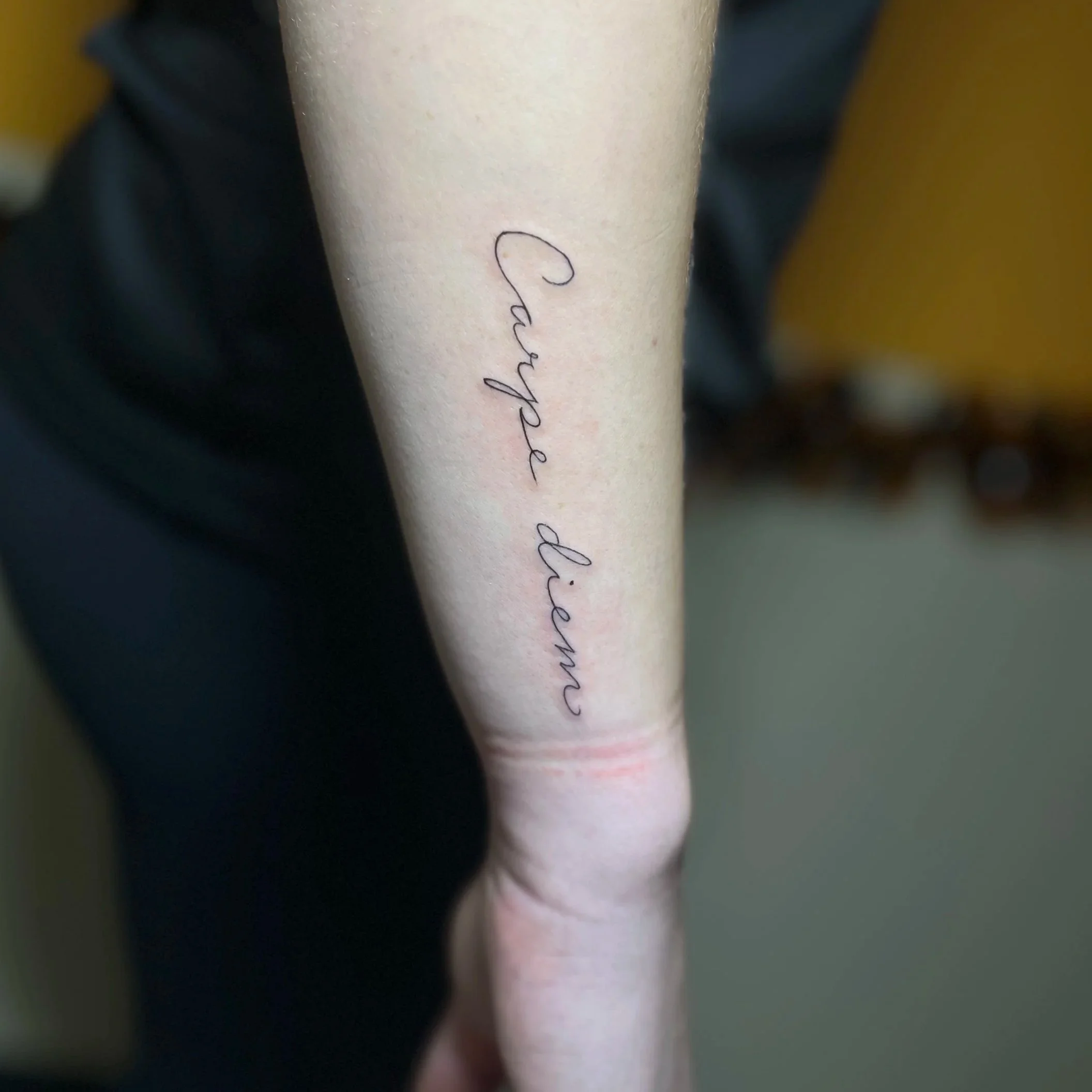 Tattoo on person's forearm that says 'Caype aliam' in cursive script.