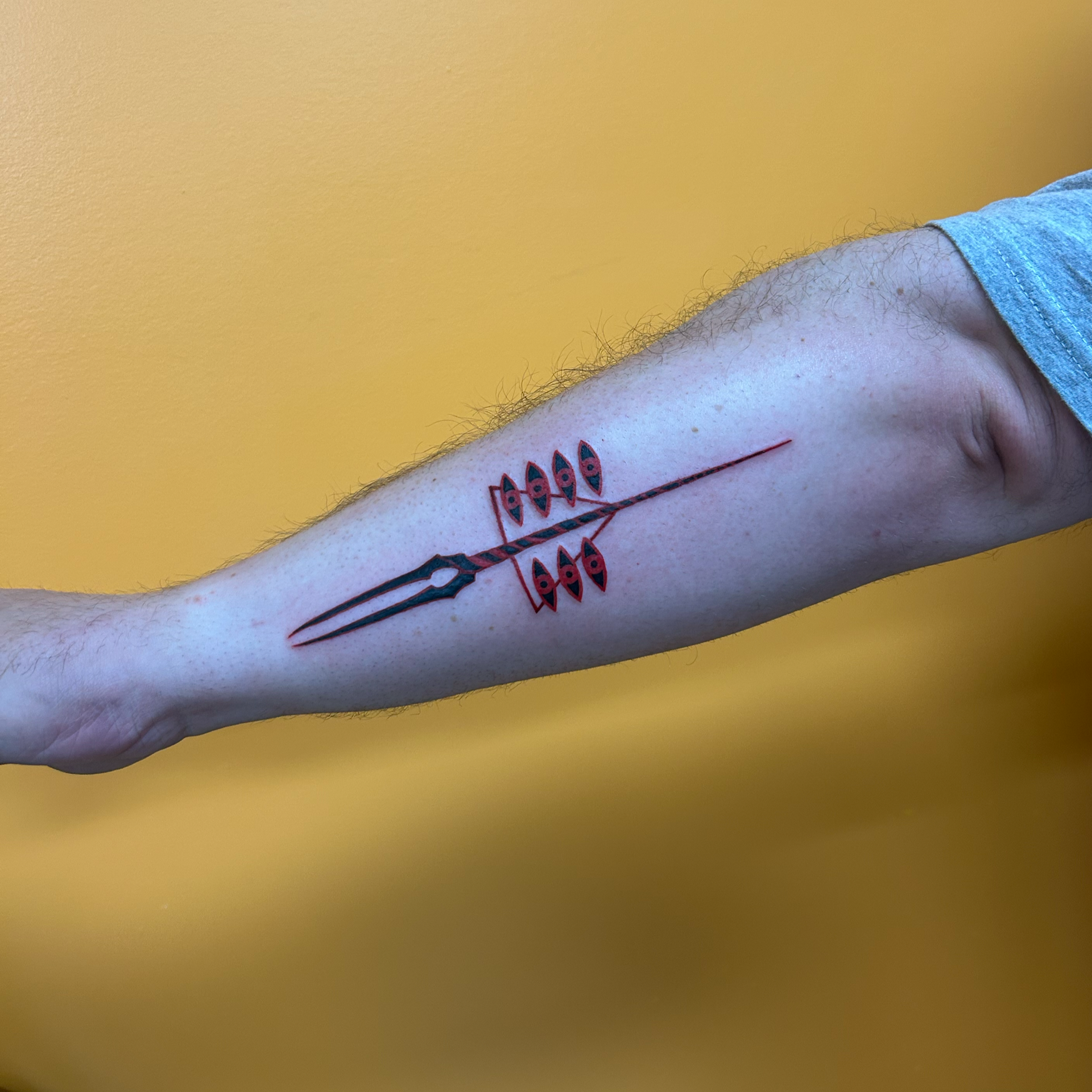 A person's arm with a tattoo of a fishing lure with six fish on a fishing line, against a yellow background.