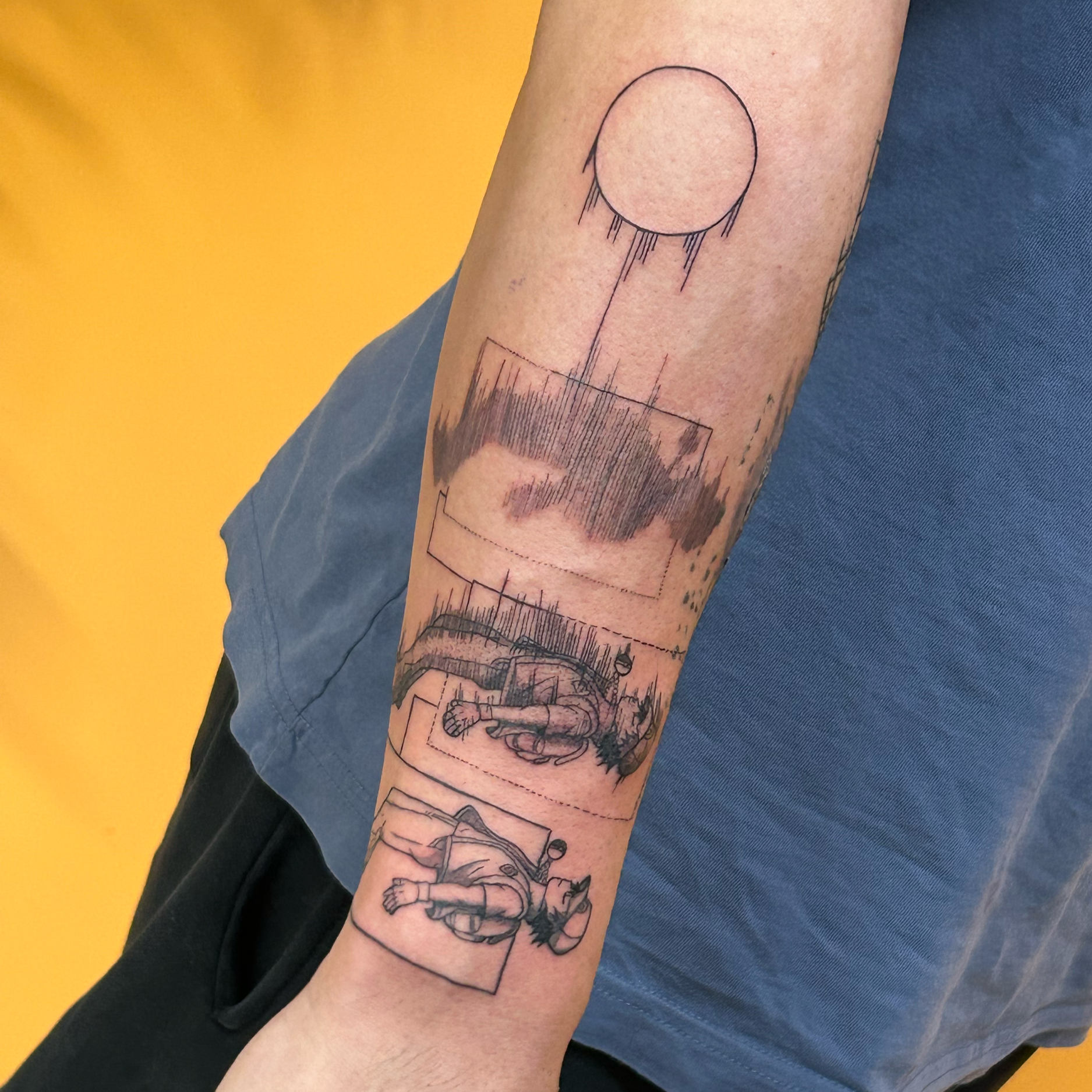 Tattoo of a large moon and several landscape sketches on a person's forearm, with a yellow background behind the arm.