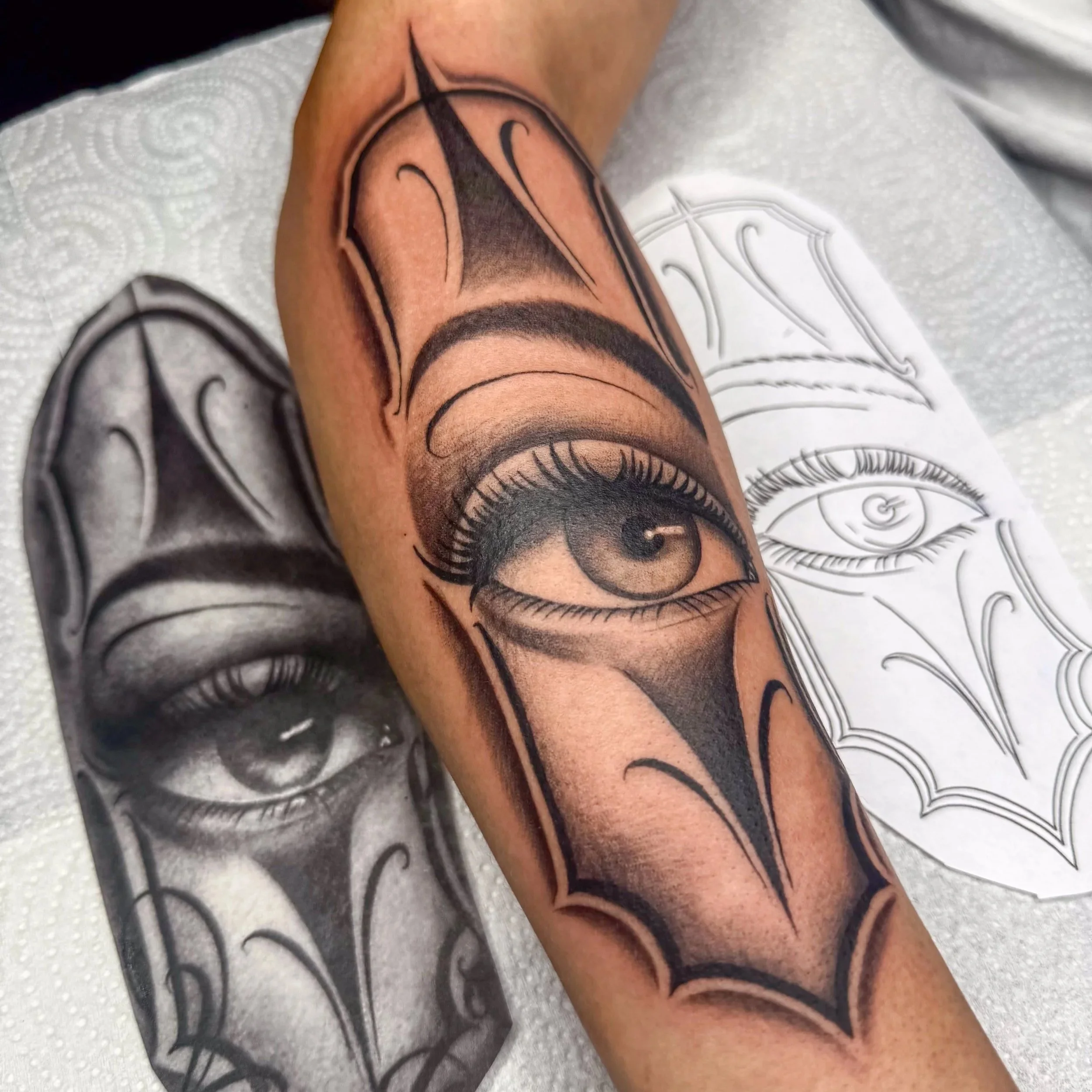 Close-up of a colorful tattoo of a woman's eye on a person's arm, lying on a white paper towel.