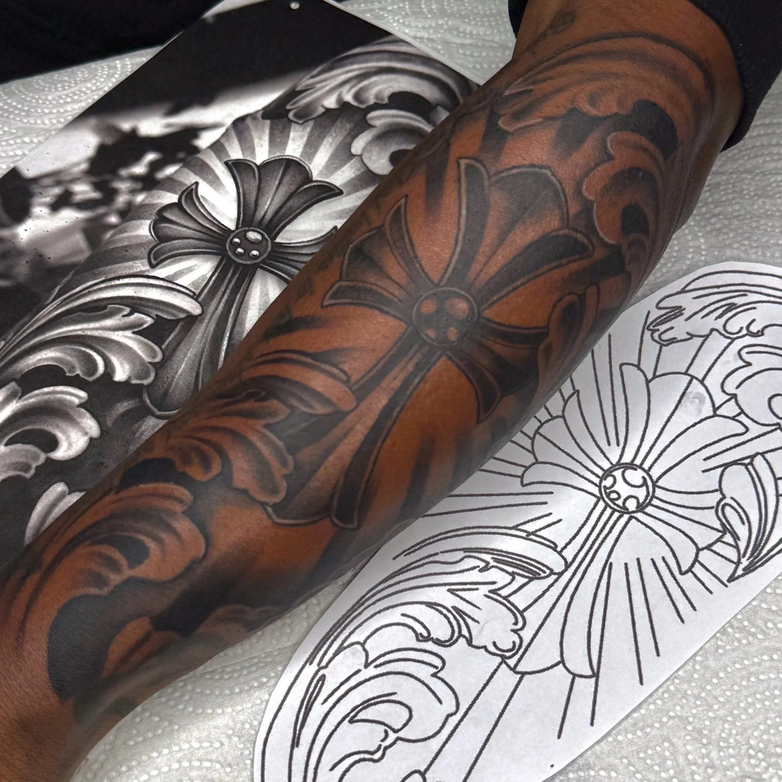 Close-up of a tattooed arm with black and brown ink, resting on a paper coloring sheet with a floral design.