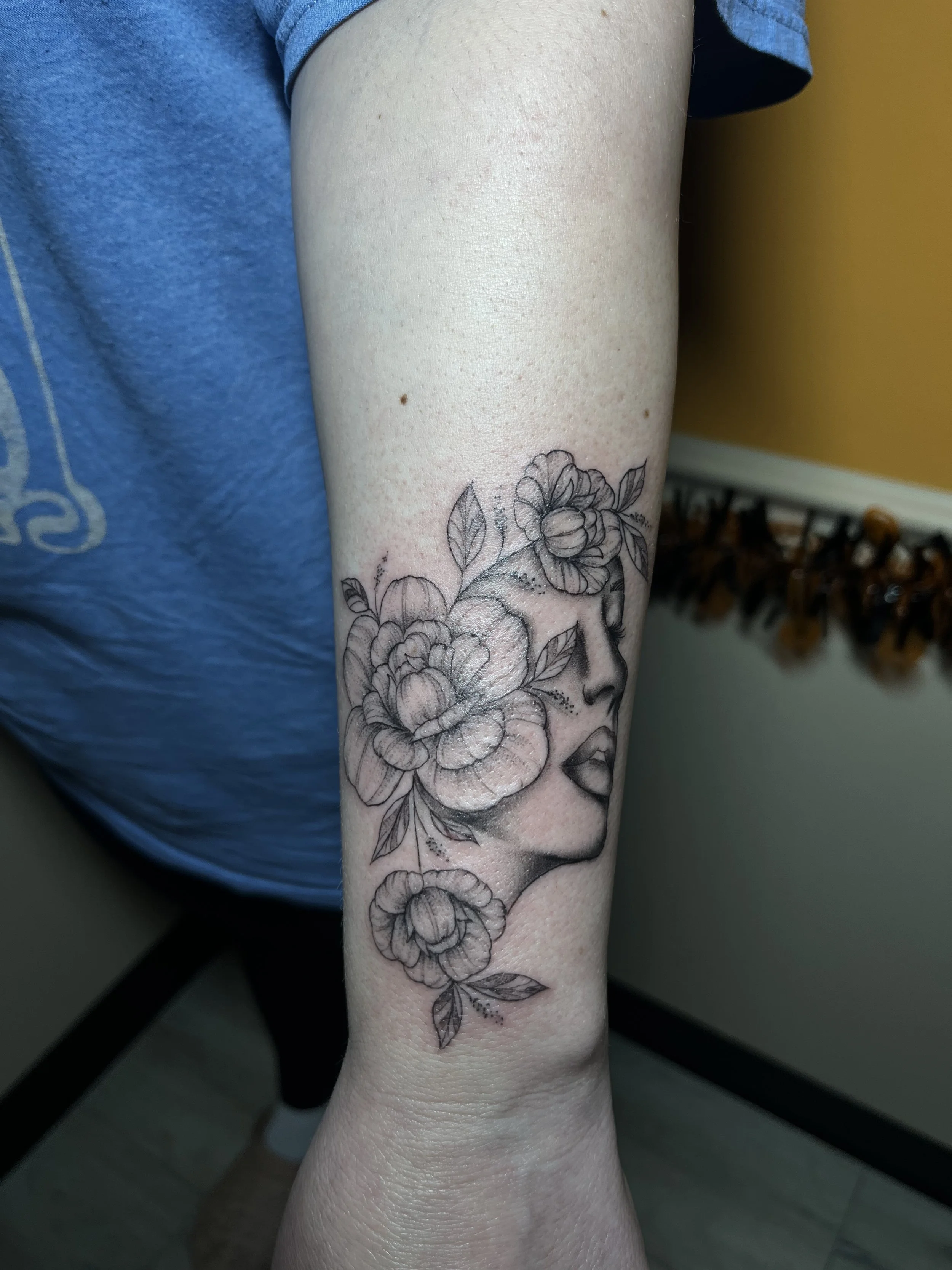 Black and gray tattoo of a woman's face surrounded by flowers on a person's arm.