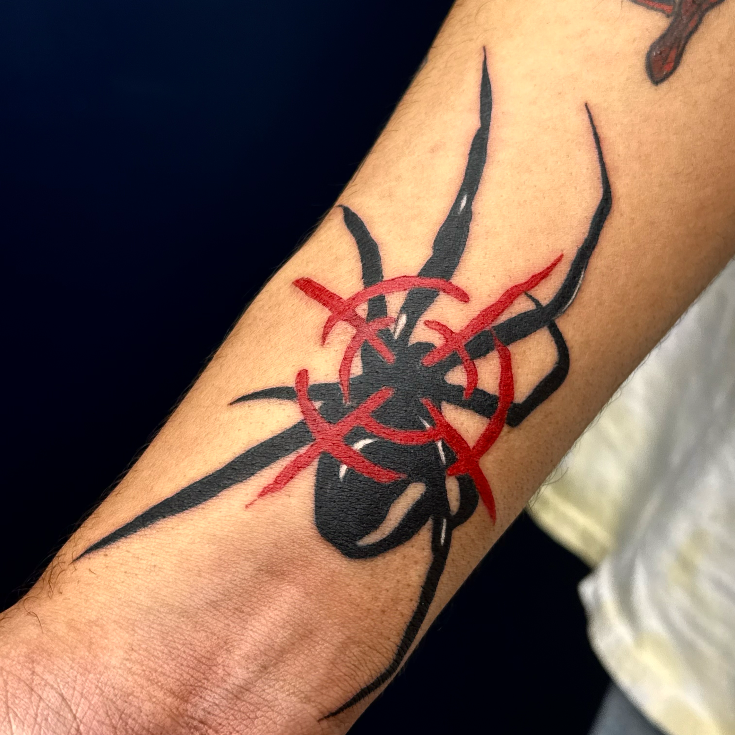 Close-up of a tattoo on a person's arm, featuring a red and black design with some line work visible.
