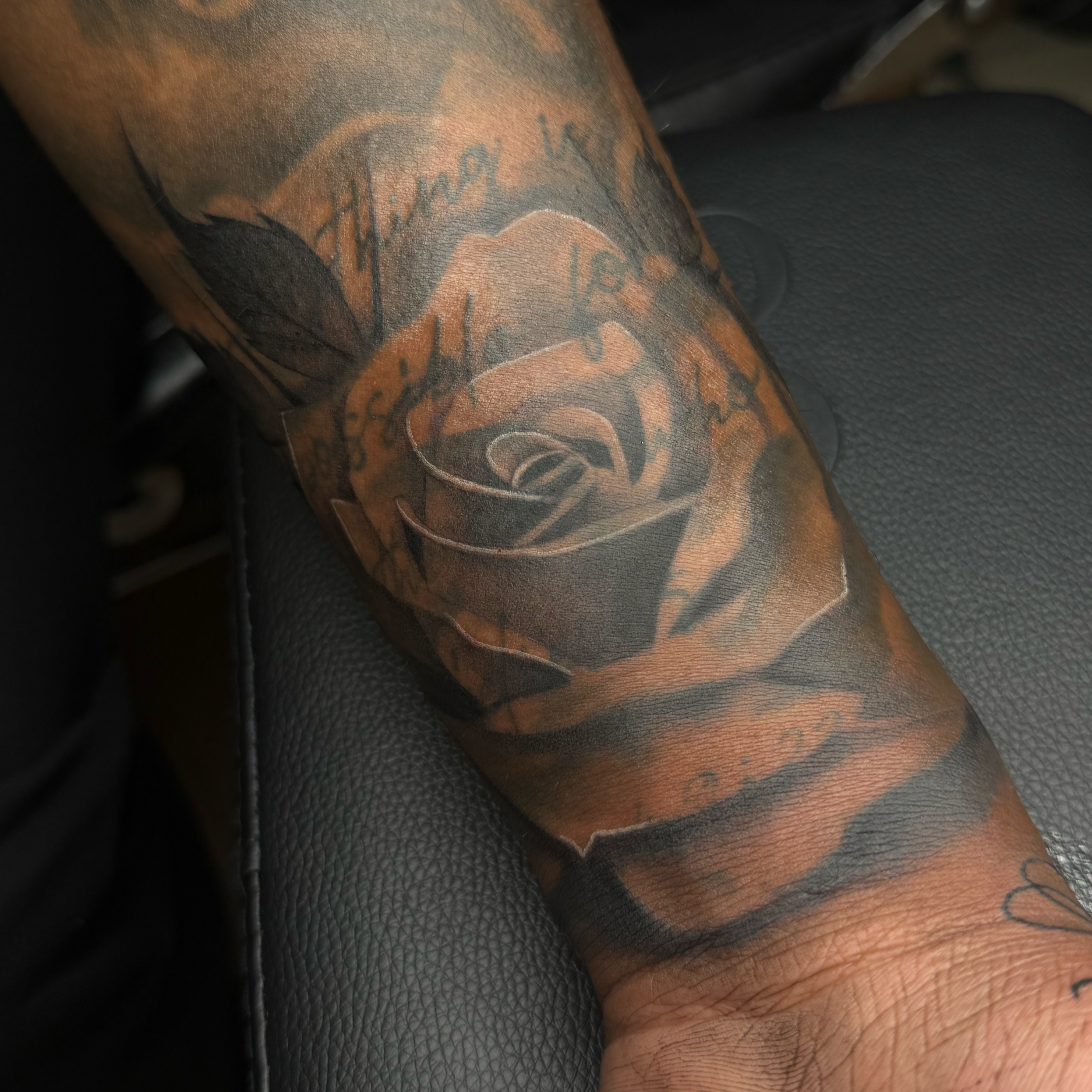 Close-up of a tattoo on a person's arm, featuring a face and text that reads 'thinking' and '176'. The tattoo is detailed with shading and color, set against the background of the person's skin and the black leather surface beneath.