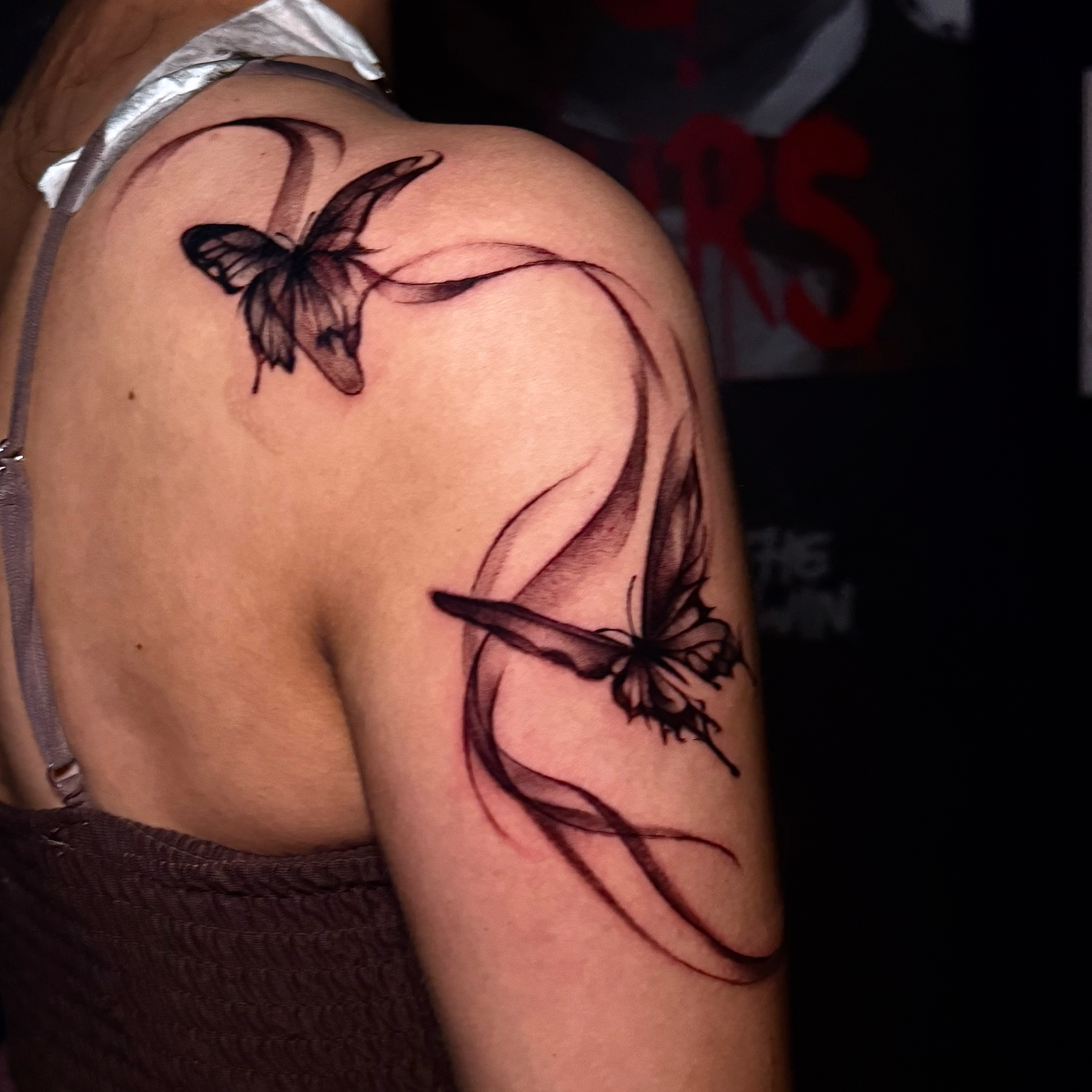 Close-up of a tattoo of a butterfly on a person's shoulder, with dark ink and intricate details.