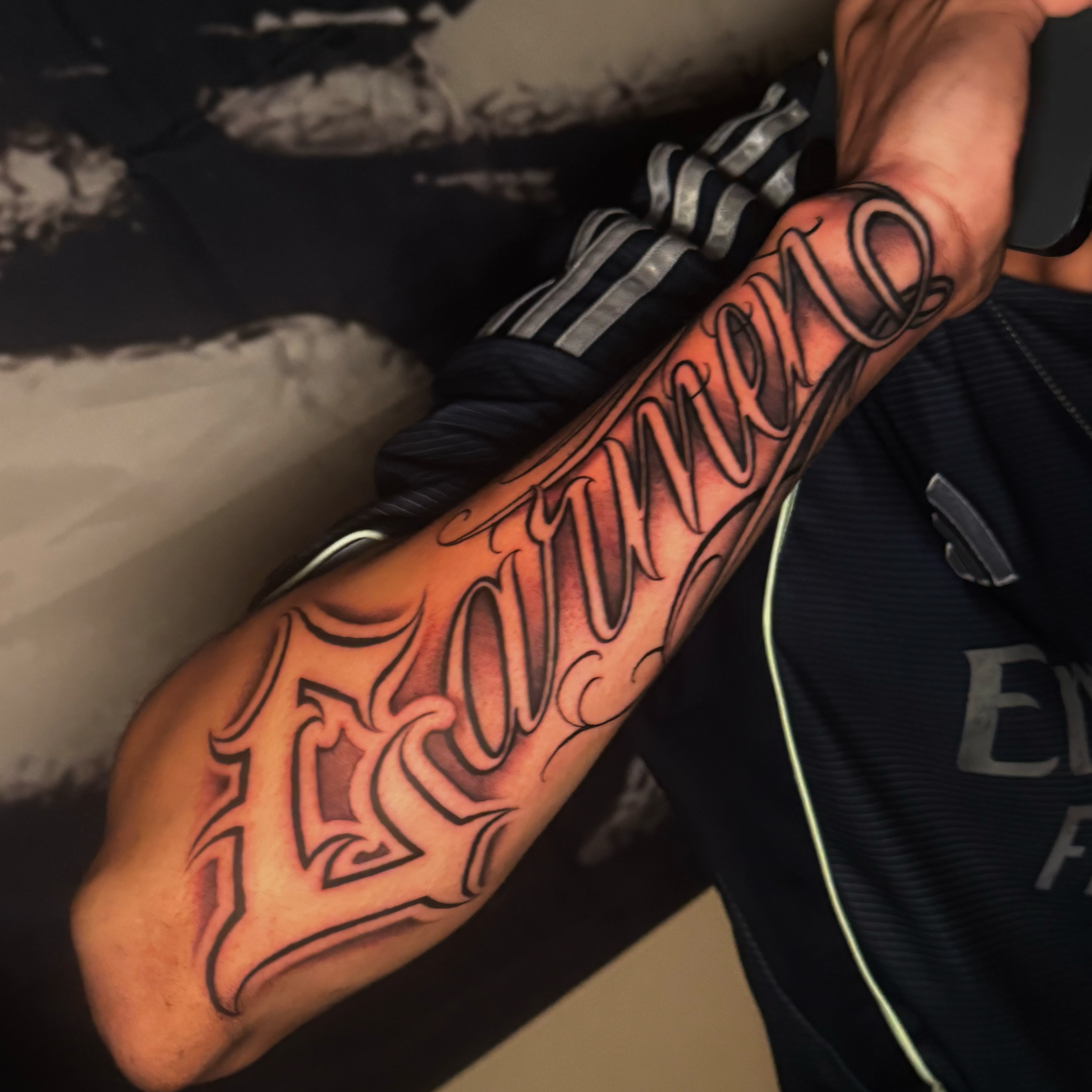 Close-up of a tattooed arm with a colorful design and black outlines, wearing a black and gray short sleeve shirt.