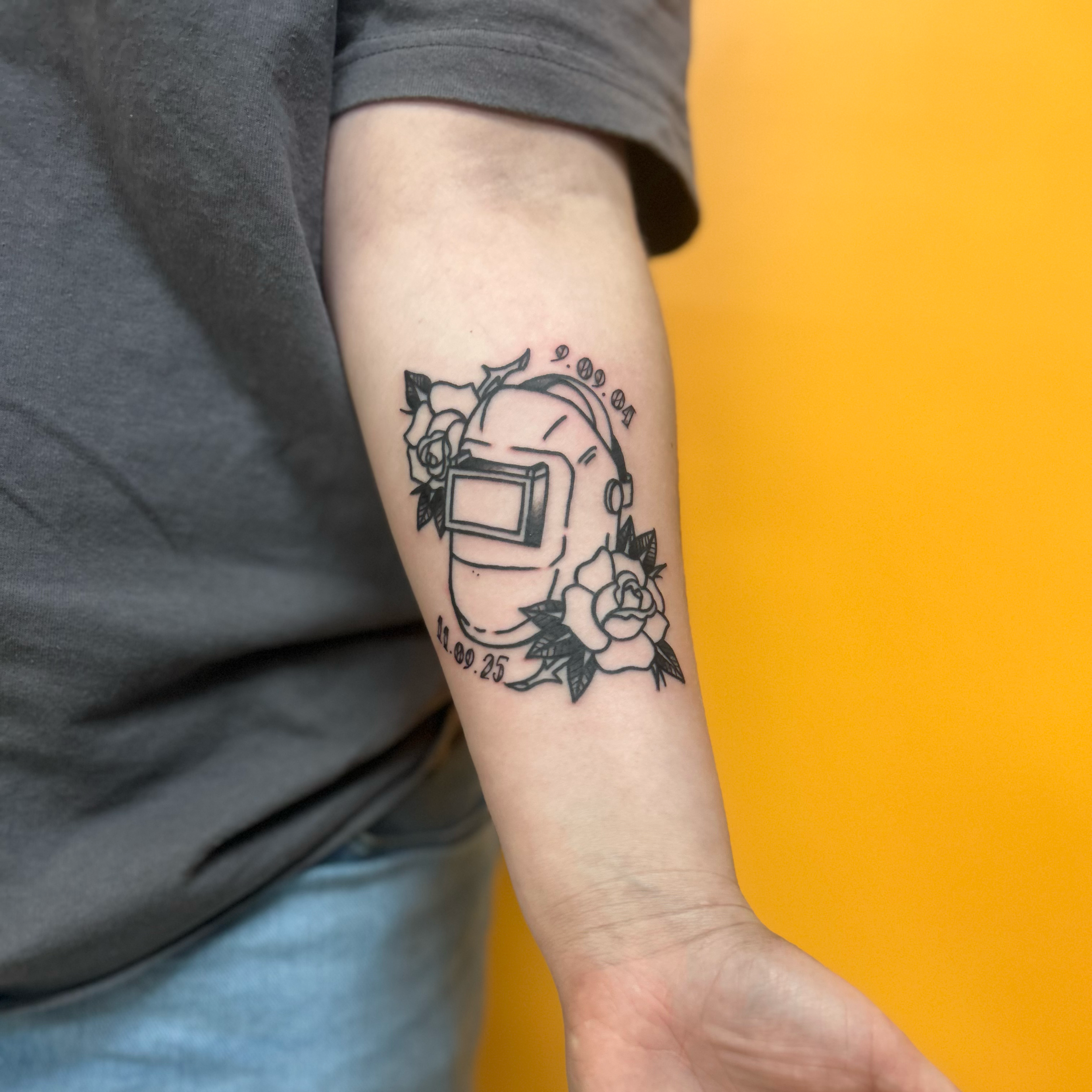 A person's arm with a tattoo showing a cartoon character with glasses, surrounded by roses, some numbers, and symbols.