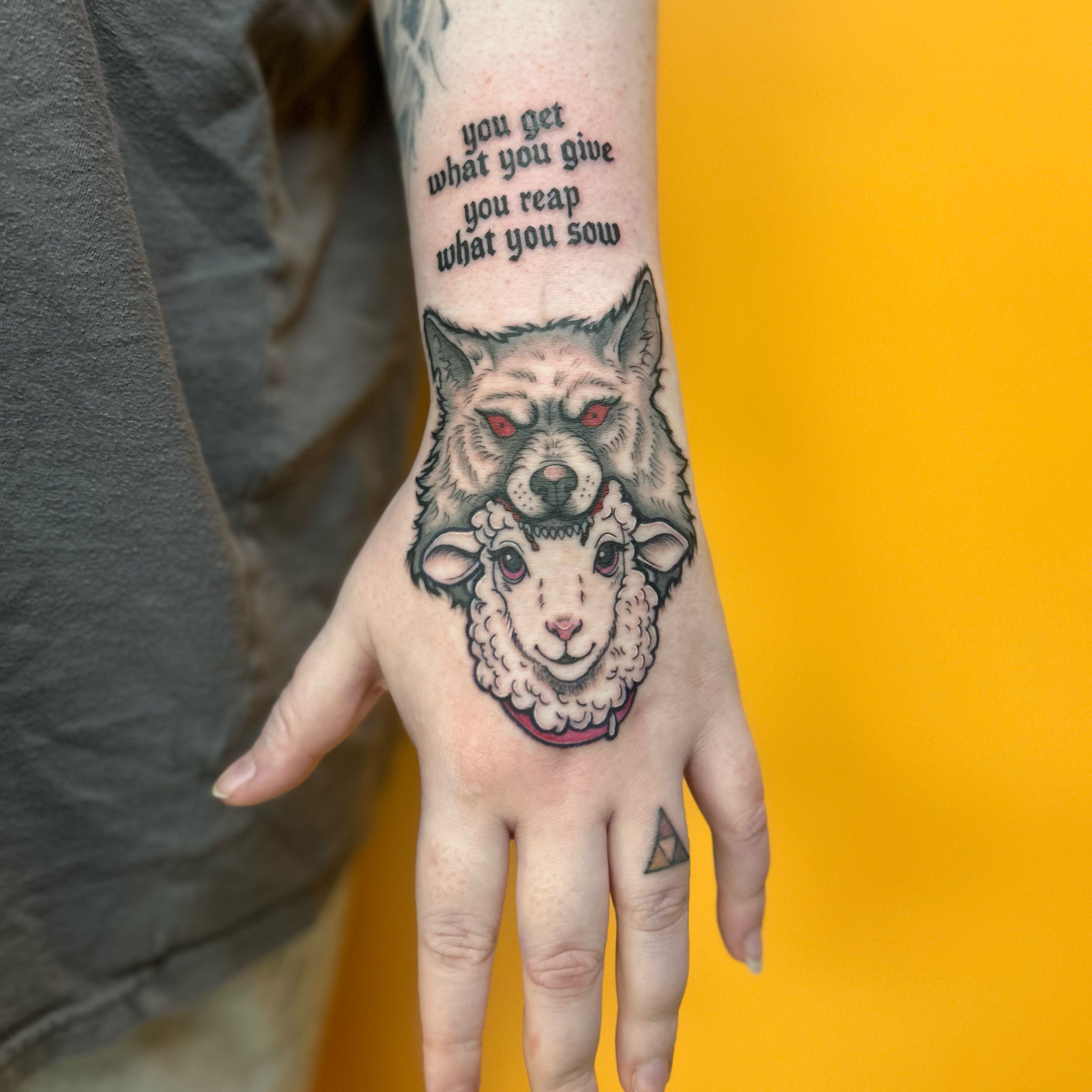 Tattooed arm with a phrase 'you get what you give you reap what you sow' and a wolf's face.