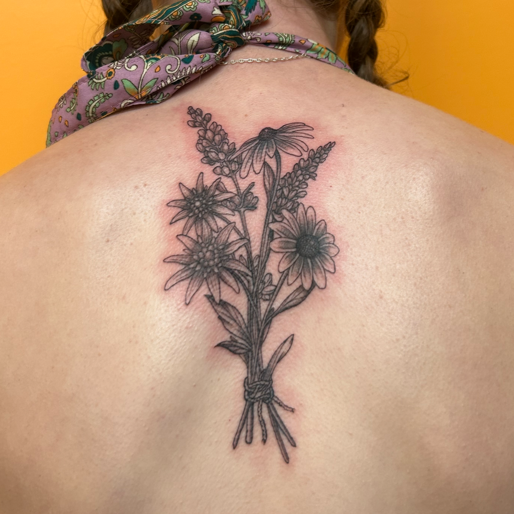 A floral tattoo of various flowers, including daisies and lavender, on a person's collarbone and upper chest, with some redness around the tattoo.