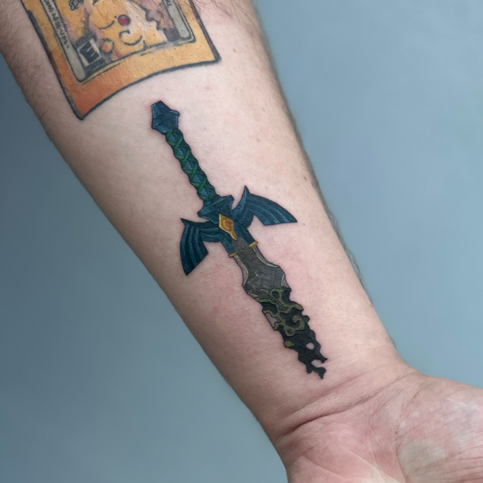 Tattoo of the map of sword on person's forearm, with a small part of another tattoo above it.