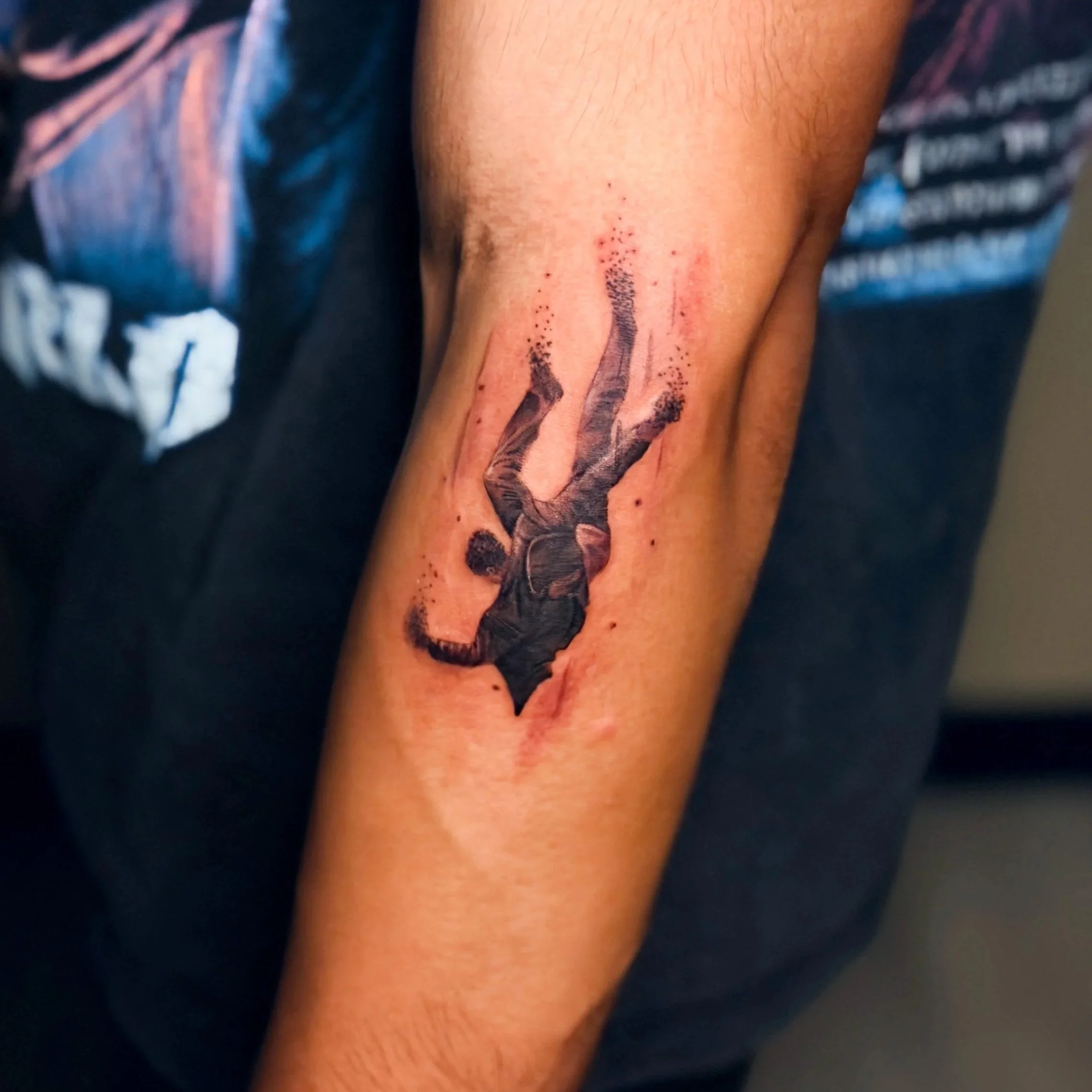 Close-up of a person's forearm with a fresh tattoo of a black ink design, a man falling 