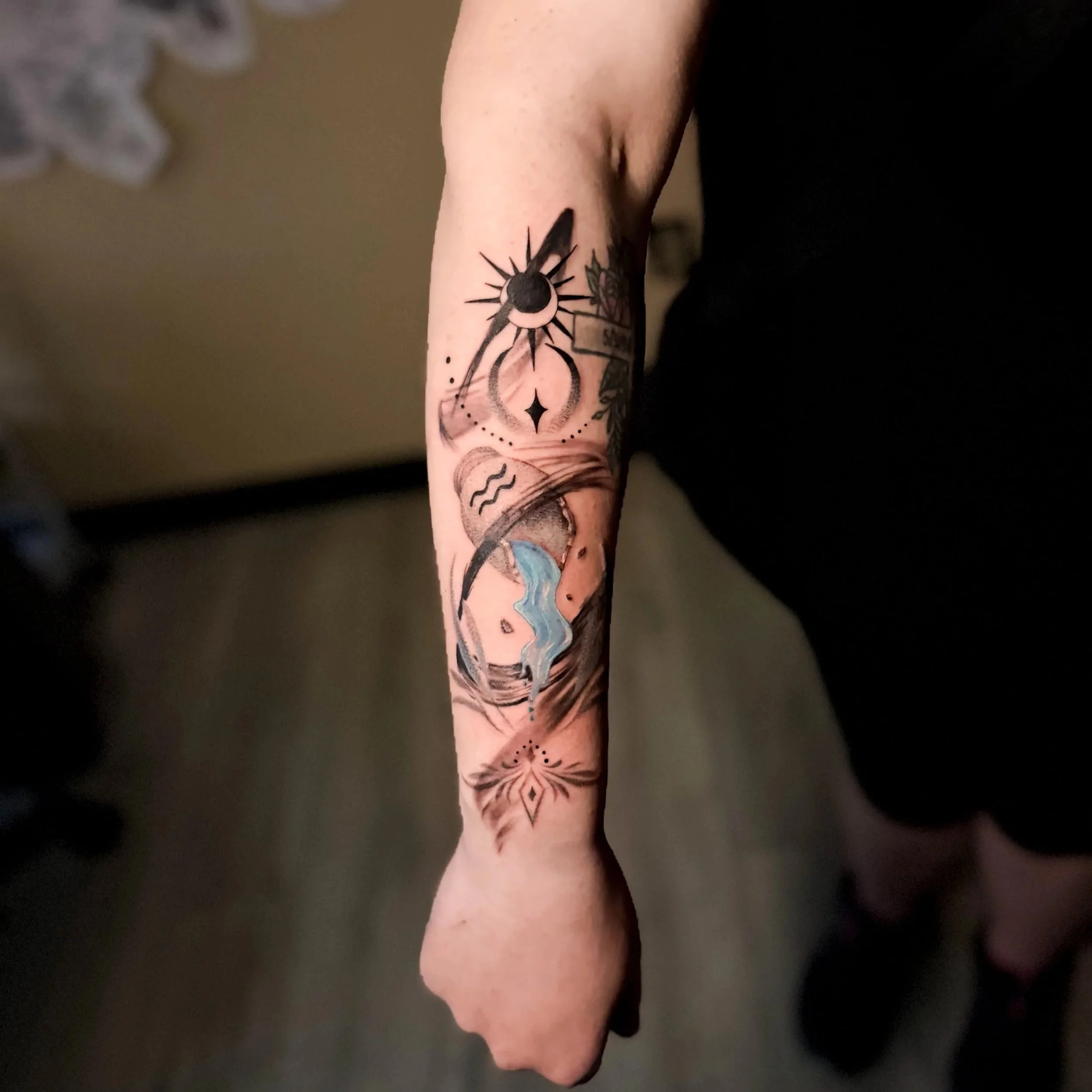 A person's arm with several colorful tattoos, including a moon and a star.