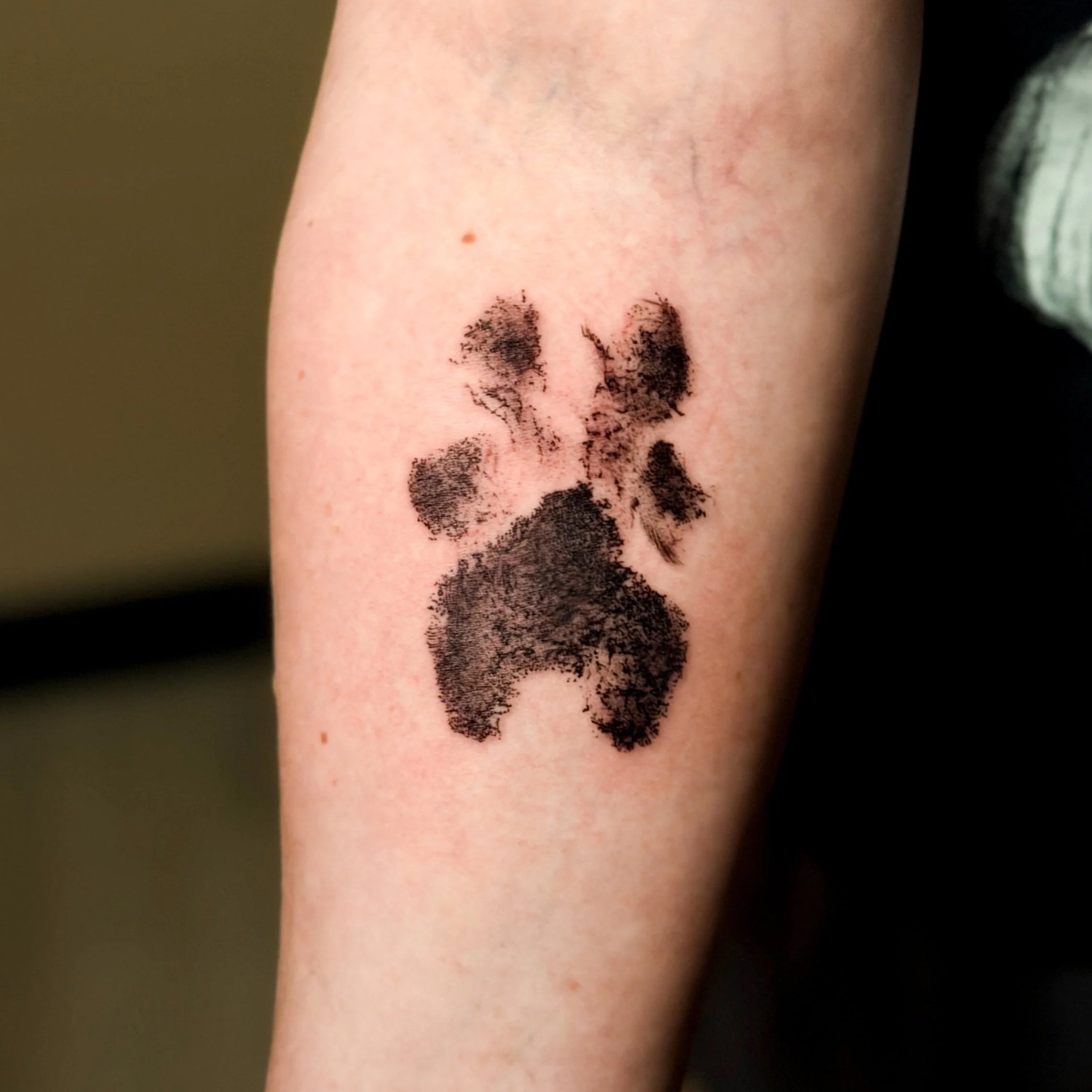 Close-up of a person's arm with a small tattoo of dog print