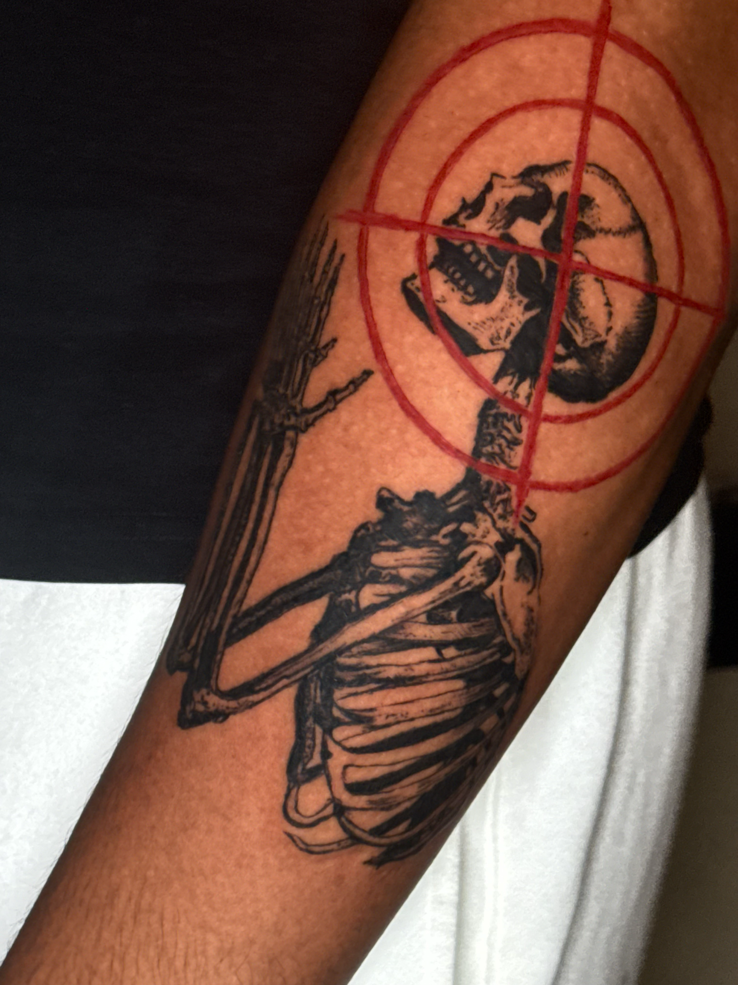 A tattoo on a person's arm depicting a skeleton riding a horse within a red circle with crosshair lines.